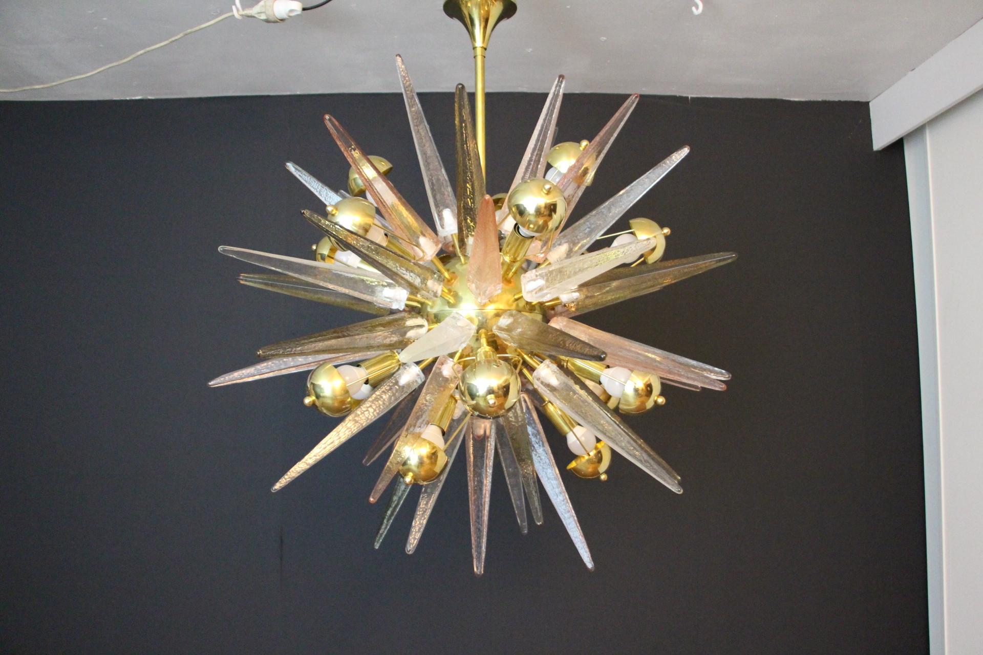 This spectacular chandelier features beautiful Murano textured glass spikes in smoke, crystal and soft pink color. Each spike is directly fixed on its polished brass central sphere.Its spikes look like ice stalactites and give to this lighting a