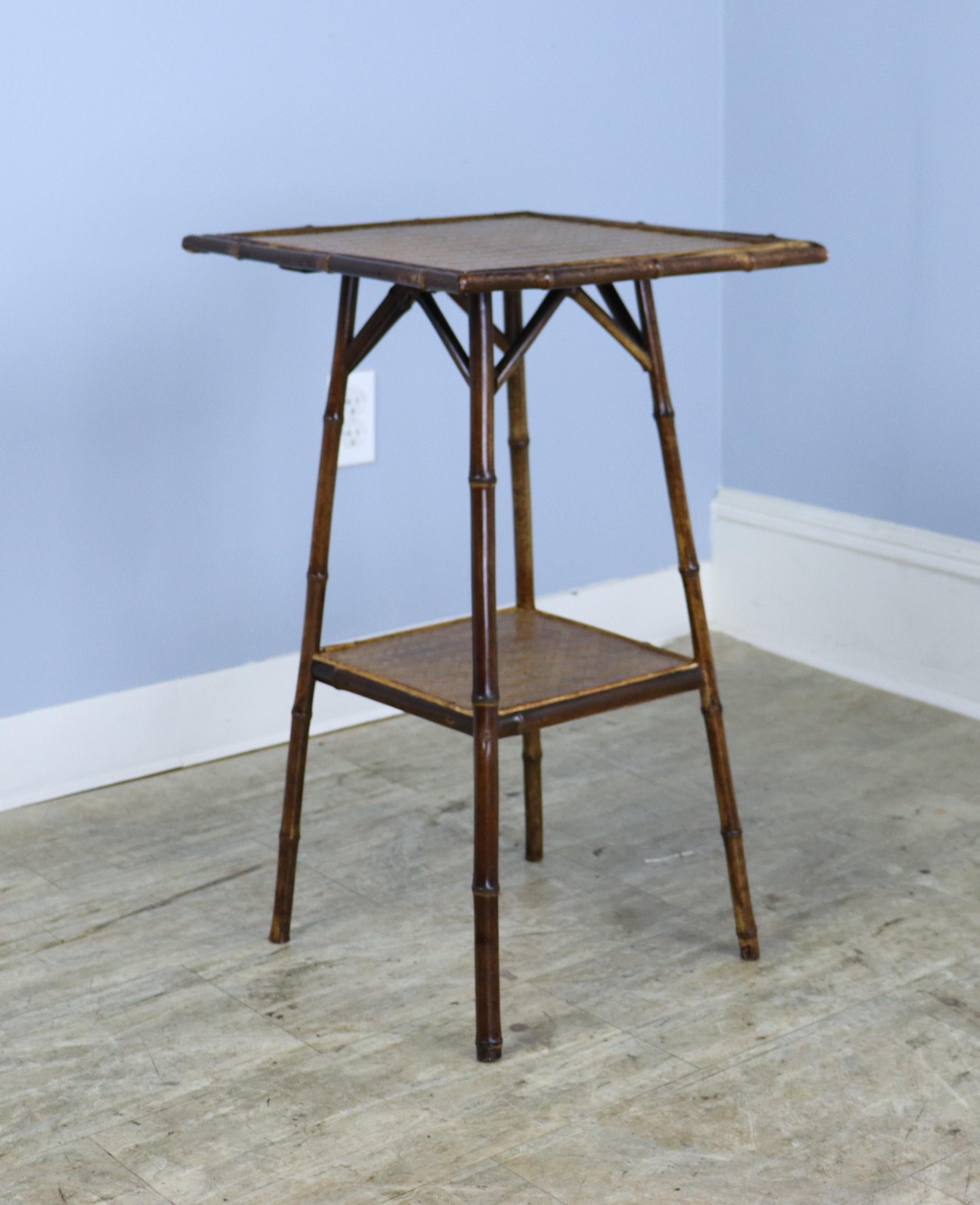 A charming bamboo side table with square top and lower shelf made of rattan in very good condition. Sturdy, and the bamboo is vibrantly colored and well constructed.