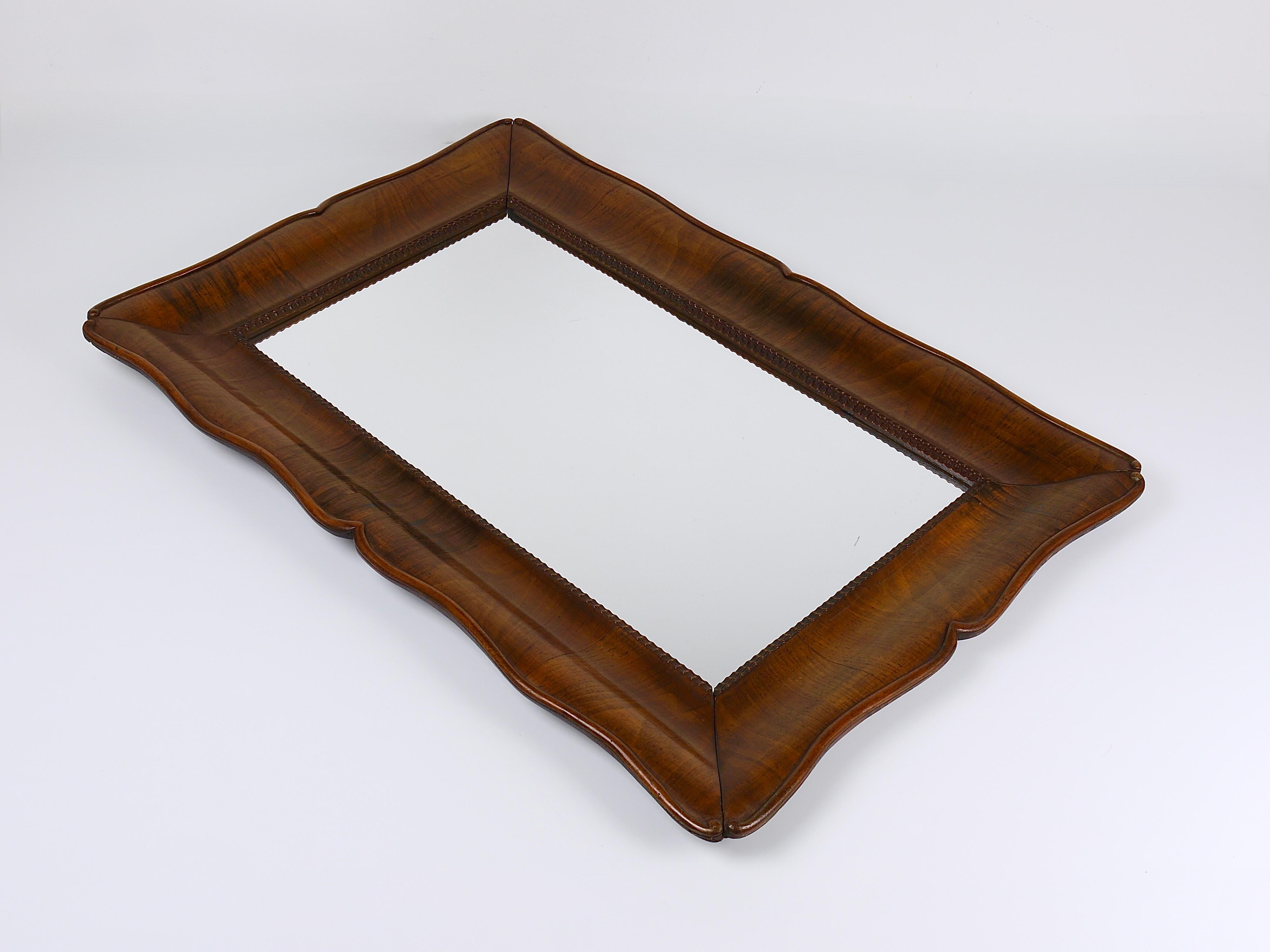 An exquisite and elegant Biedermeier wall mirror from Vienna, Austria, ca. 1850. This fine piece showcases a beautifully profiled and gracefully scalloped walnut frame, distinguished by its rich, deep grain and refined curvature. It remains in good