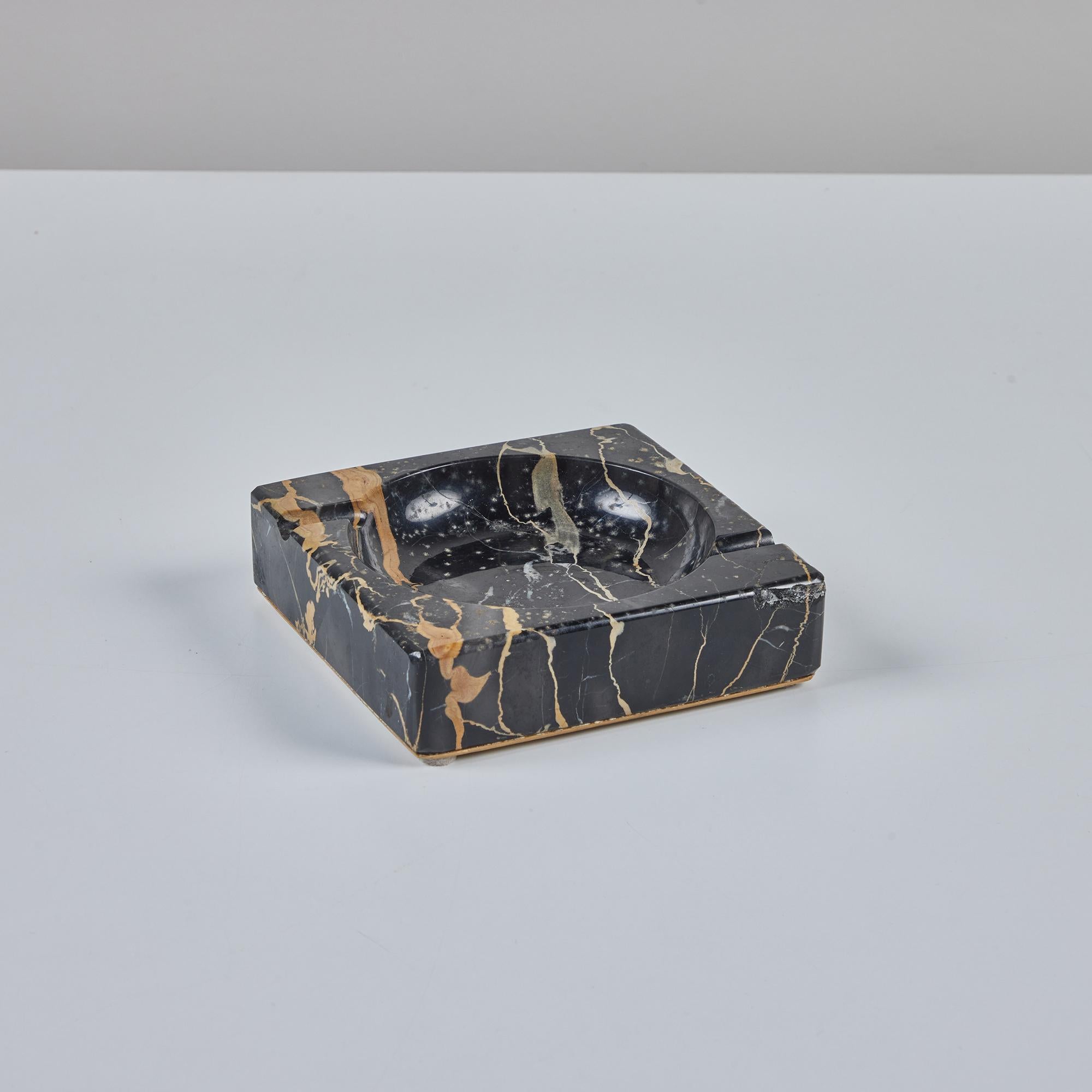Square marble ashtray in a polished black marble with cream and tan veining by the Candoro Marble Company of Knoxville, Tennessee founded in 1914. The piece has a circular well, and two routed asymmetrical indentations perpendicular to its edges.