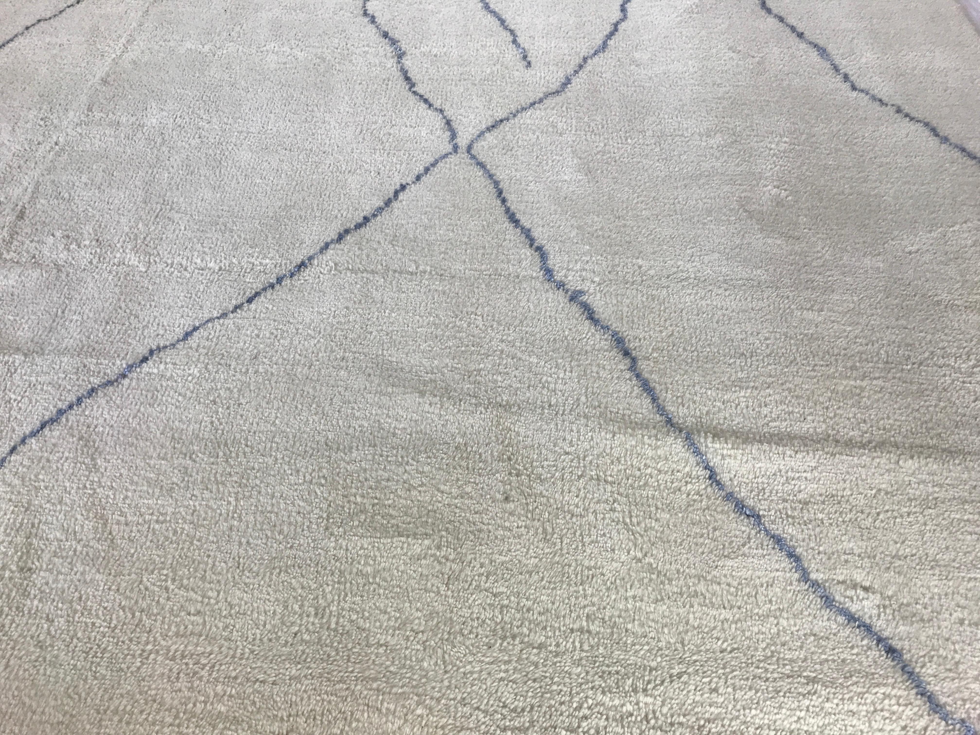 Dieser fast quadratische, cremefarbene Teppich zeichnet sich durch eine kühne blaue Linie und ein kompliziertes, marokkanisch inspiriertes Muster aus, das aus hochwertiger Wolle gefertigt ist. Mit seiner einzigartigen Mischung aus Stil und