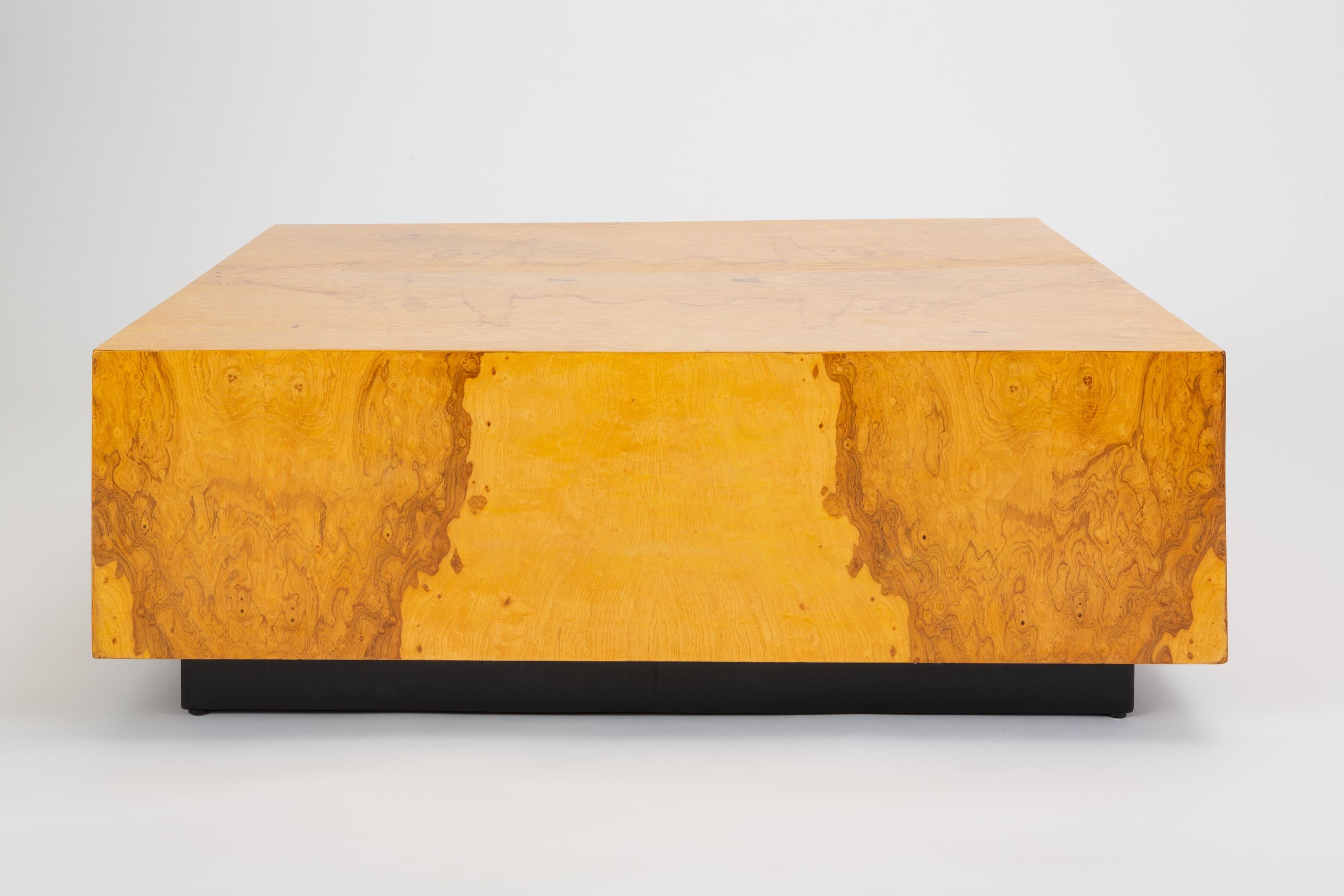 A late 1970s square coffee table on a black plinth base. The surface of the large piece is veneered in bookmatched burl wood. We have a matching pair of side tables available as well. 

Condition: Excellent vintage condition; refinished but some