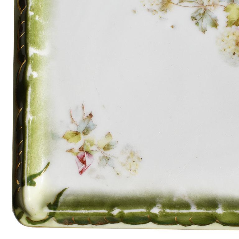 A beautiful square hand-painted decorative trinket dish or ashtray. This ceramic piece is flat, and perfect for a dressing table or nightstand. The edges are painted in a deep green with gold detail. The center features pink roses amongst lush green