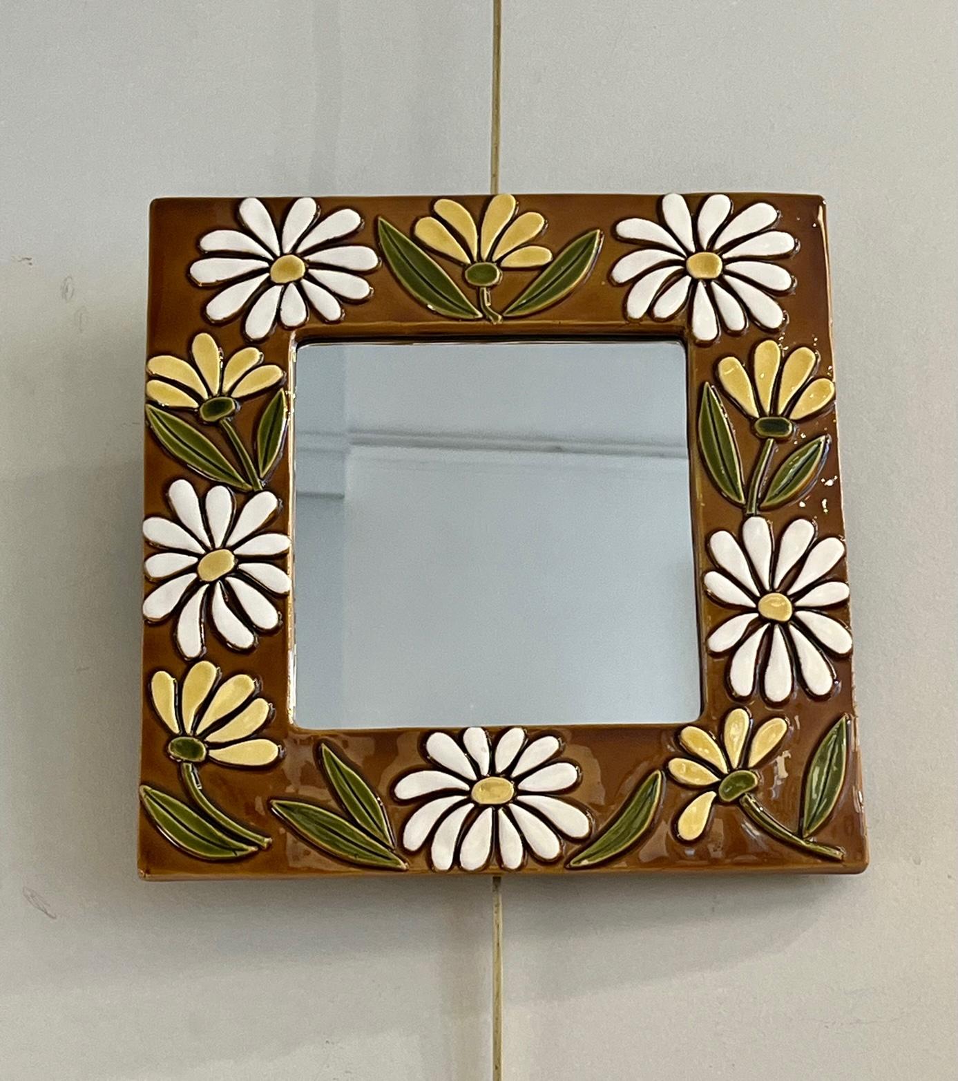 Square ceramic mirror by Mithé Espelt 
The  broad glazed ceramic frame is decorated with white and yellow daisies and foliage on a light brow background. 
This type of design is rarely seen in Mithé Espelt's work although flowers were one of the