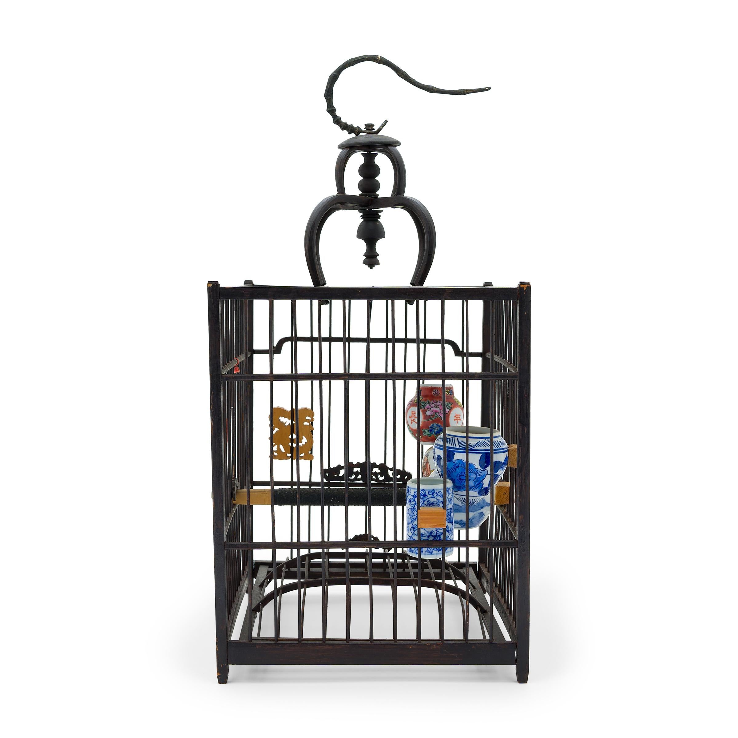 This delicate wooden birdcage was once home to the tiny pet bird of a Qing-dynasty aristocrat. Dated to the Mid-19th Century, the square cage is precisely assembled from thin bamboo rods and has a removable base, a large metal hook, and a sliding