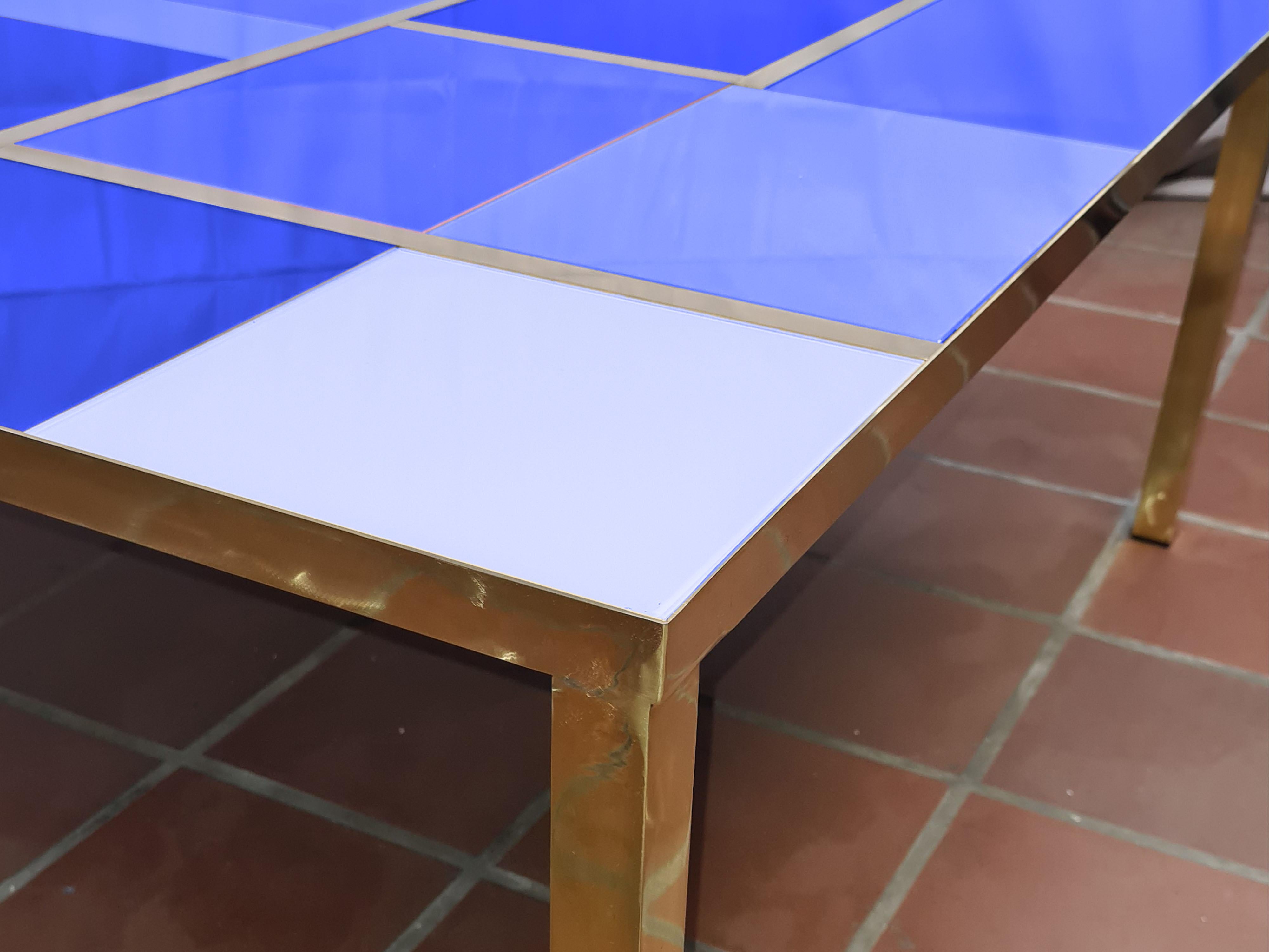 Esta mesa de centro cuadrada con cristal de Murano azul espejado y adornos de latón es una impresionante pieza de diseño moderno, fabricada a mano en Italia. 

Su llamativa encimera de cristal azul con diferentes tonalidades del mismo color presenta