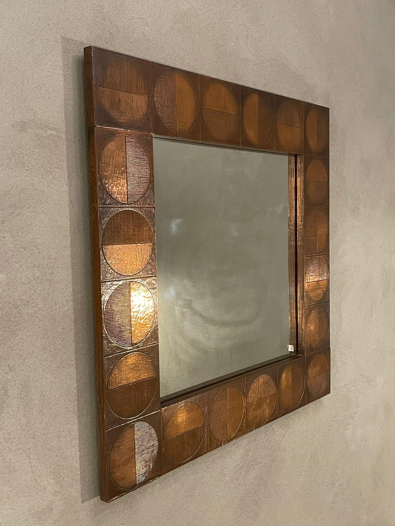 Square copper mirror manufactured in Italy, 1960s.
Square frame in copper decorated with the presence of twenty small squares, each of which containing a circle. 
A semicircle in a different position, in each square, appears decorated with