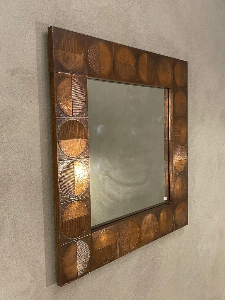 Square copper mirror manufactured in Italy, 1960s.
Square frame in copper decorated with the presence of twenty small squares, each of which containing a circle. 
A semicircle in a different position, in each square, appears decorated with
