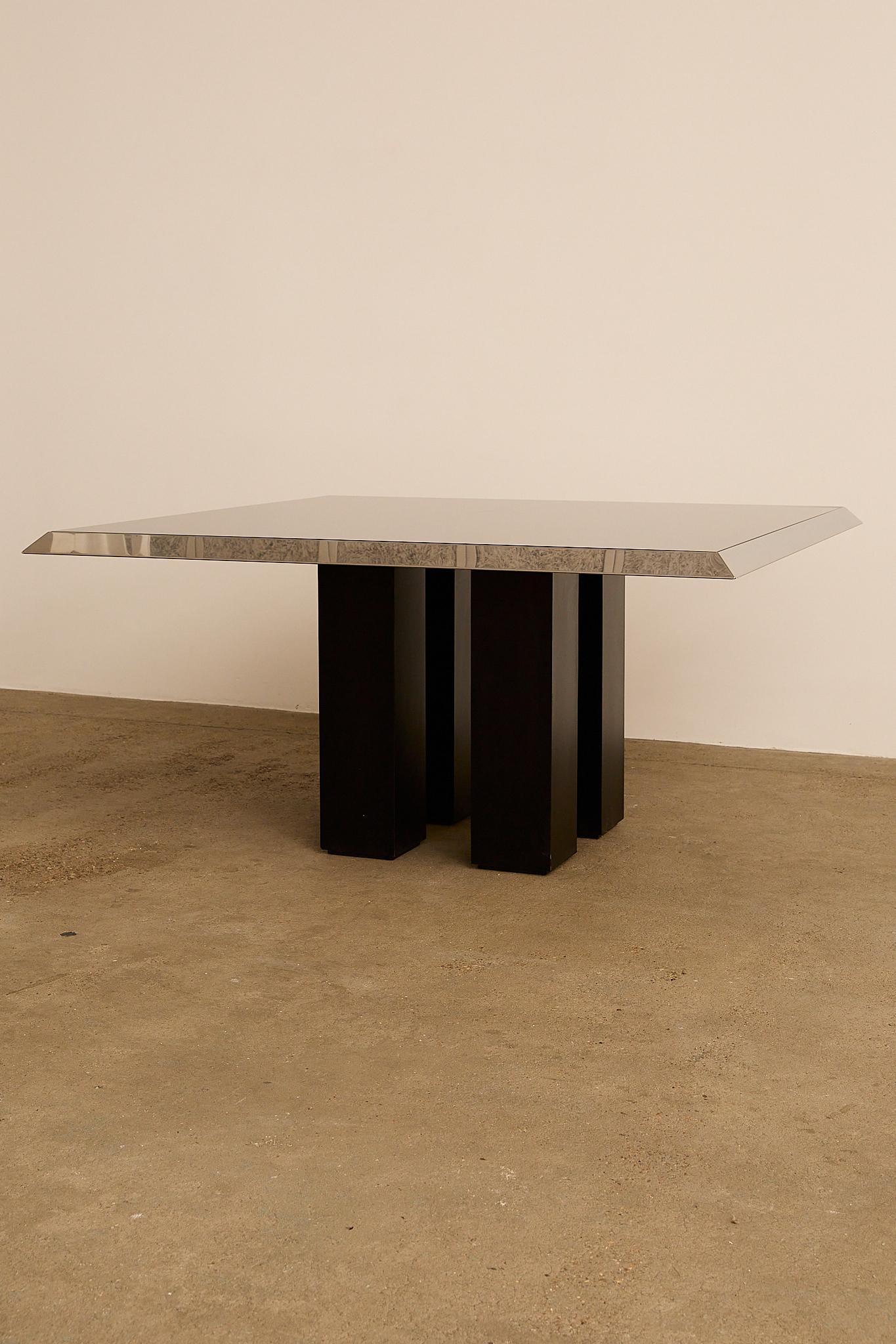 Table de salle à manger italienne des années 1970, avec un plateau en verre fumé encadré de chrome poli. La base sculpturale est constituée de quatre piliers laqués noirs, ce qui confère à la pièce une forte présence architecturale. Veuillez noter