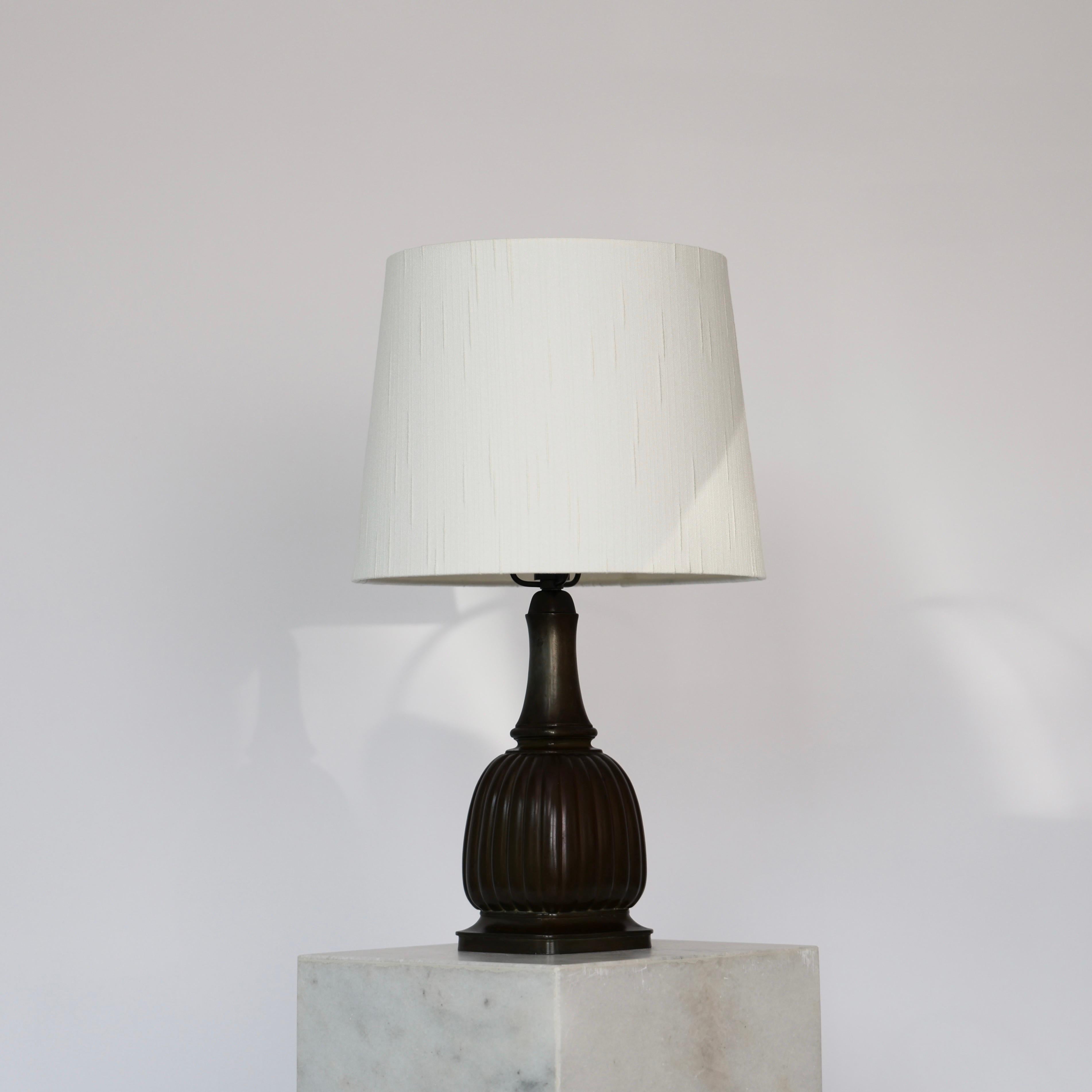 Timeless no. 1856 Table Lamp made by Just Andersen in the 1930s.
 
* Discometal table lamp with a square cannellated body, slim neck and white shade.
* Designer: Just Andersen
* Model: 1856
* Year: 1936
* Condition: Good vintage condition. Makers