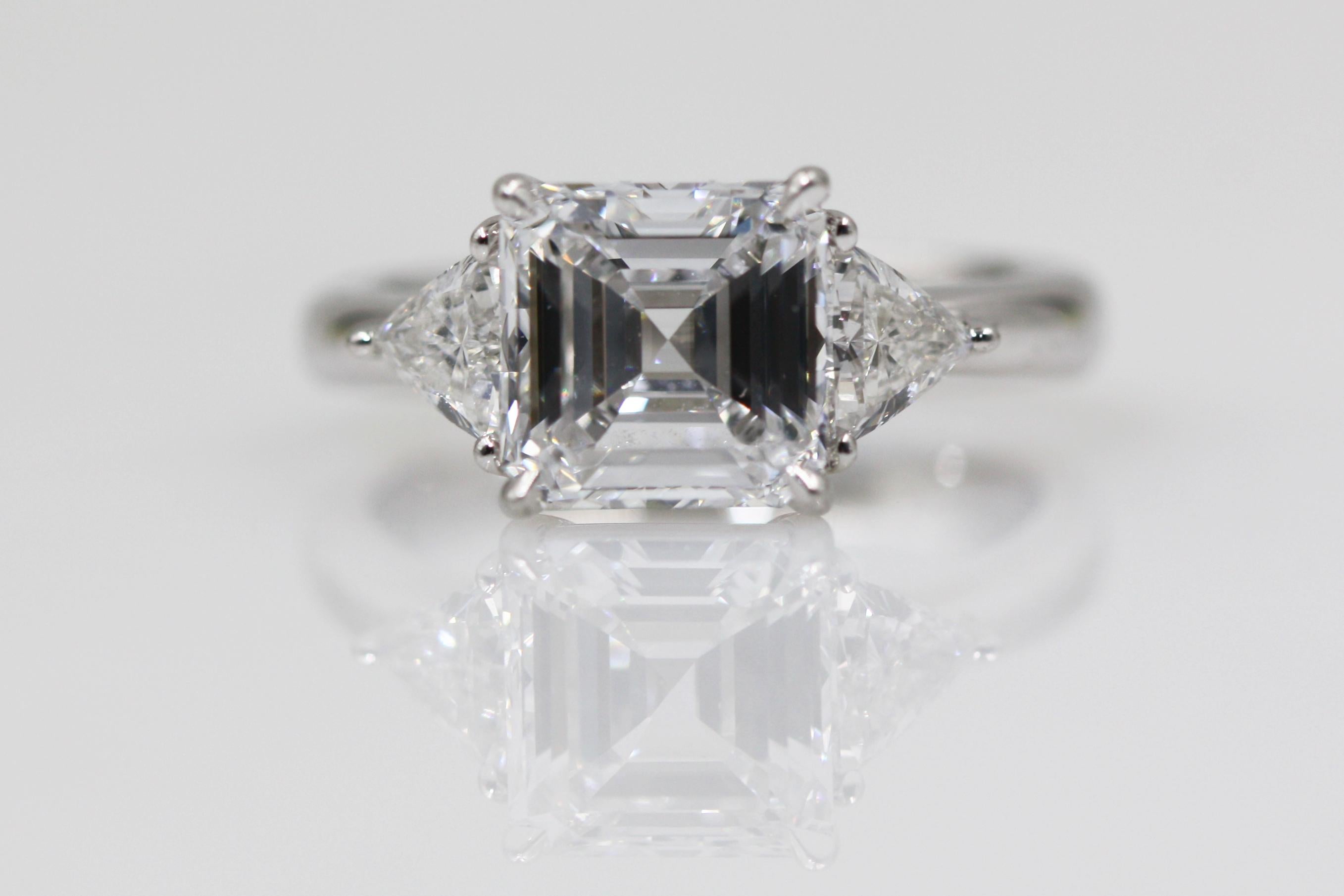 A square emerald-cut engagement ring, 2.27 carats, with trilliant-shaped diamond side stones weighing a total of approximately 0.52 carats, set in platinum. This timeless engagement ring showcasing the natural beauty of rare diamonds and precious