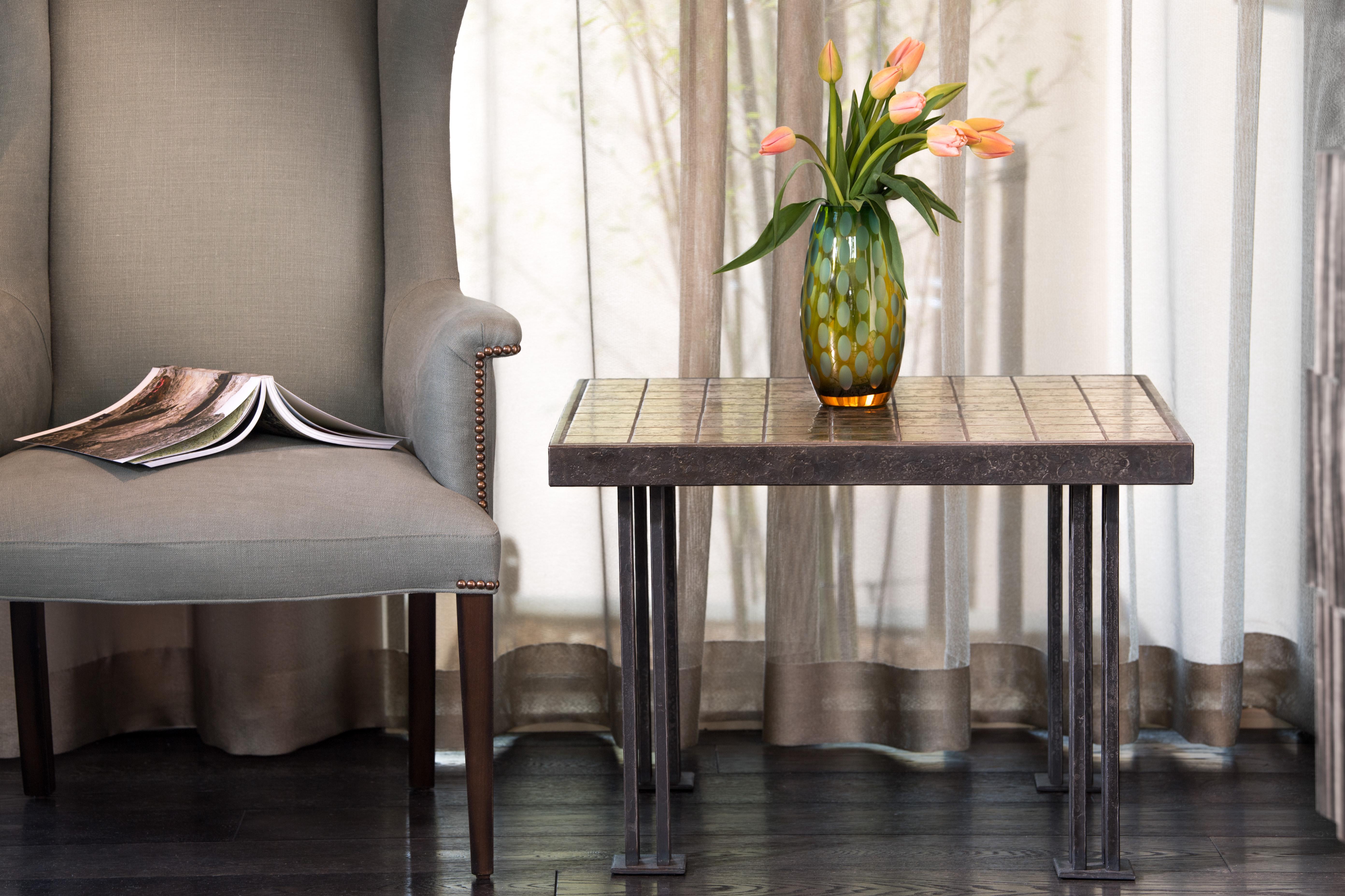 The table top of this square end table is composed of individually forged bronze tiles surrounded by a forged steel frame. The bronze tiles have a burnished finish that accentuates the unique surface of each tile. Hand-forged legs are created from