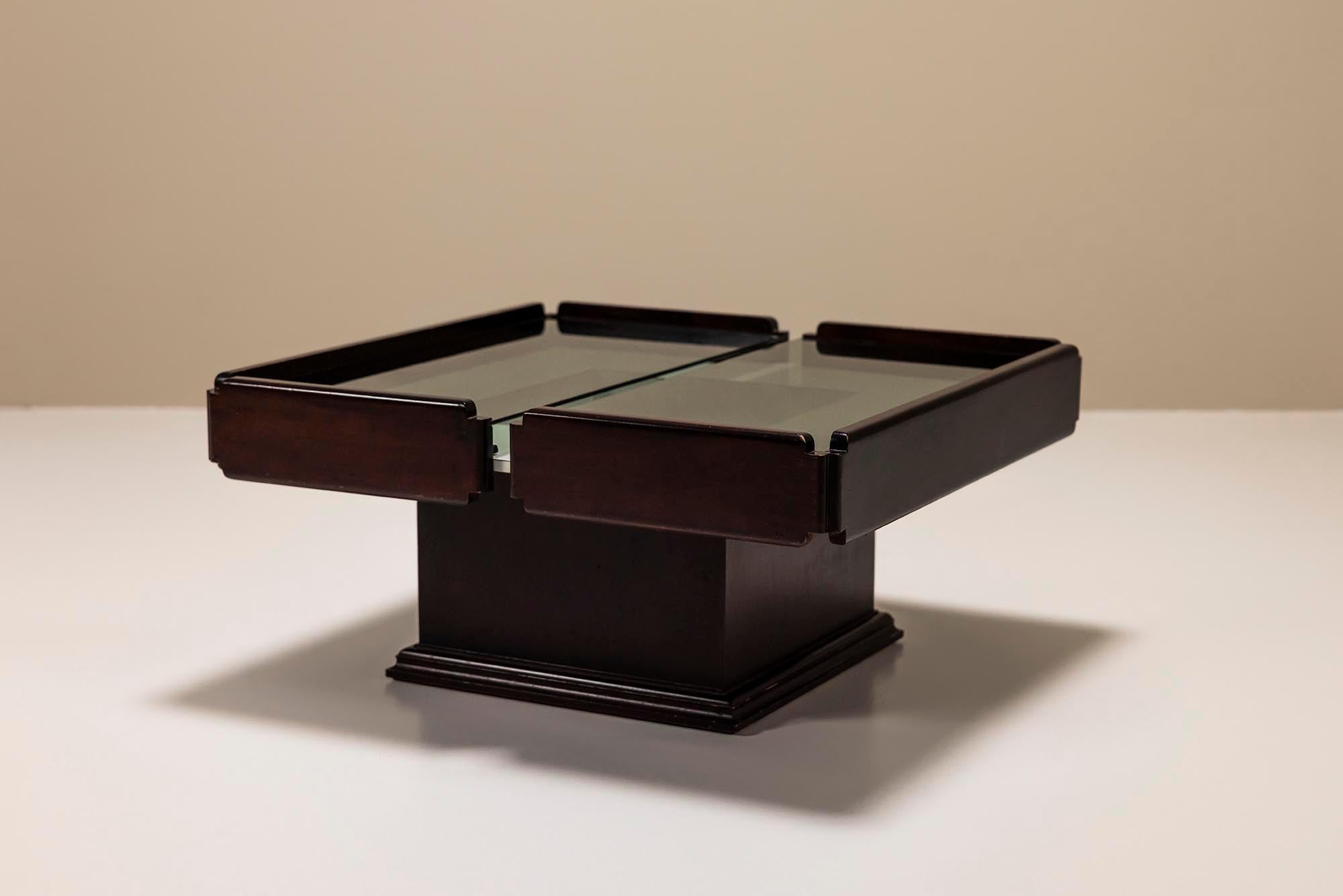 Cette table basse datant des années 60 présente une combinaison agréable de deux styles différents. La base peut être décrite comme carrément classique, presque une sorte de colonne, tandis que les panneaux en bois créent une forme plus moderniste.