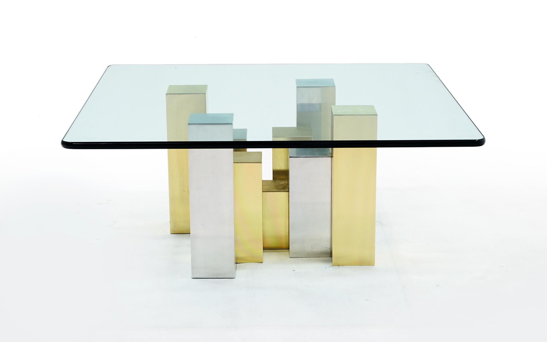 Coffee table in the style of Paul Evans with a glass top and cityscape style base in brushed chrome and brushed brass.