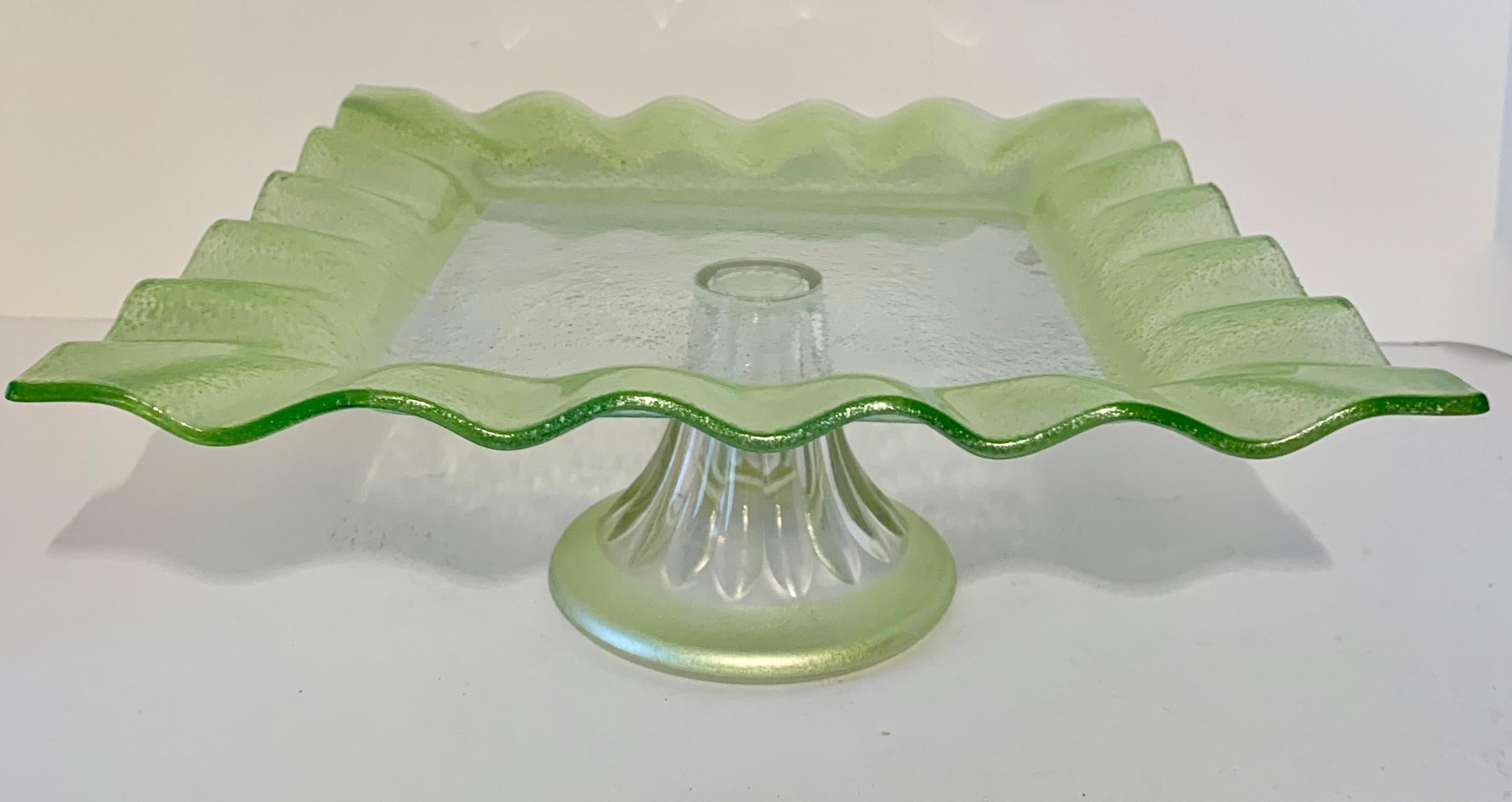 A square glass footed cake or pastry display plate with glass 'Ruffle' around the perimeter. The footed plate is made of glass that has been tinted Celadon around the edge of the Ruffle detail and Base... wonderful for displaying cakes or other