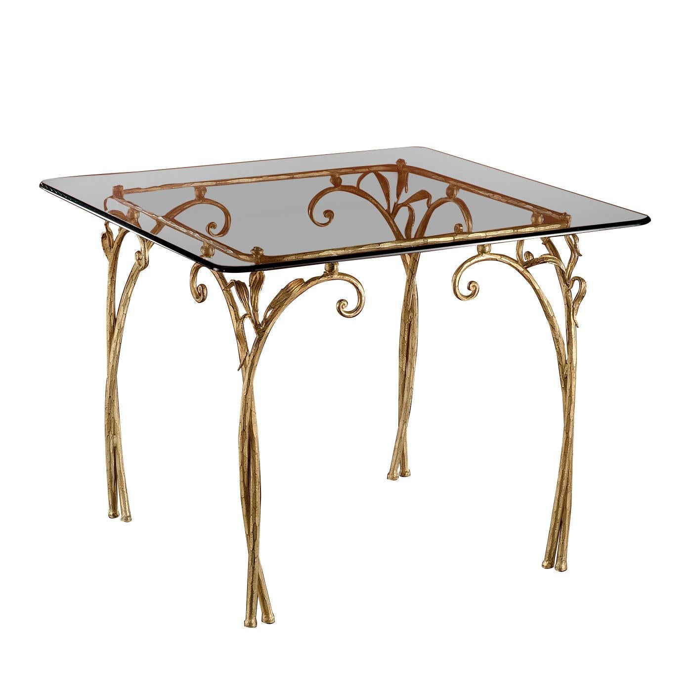 A magnificent example of masterful craftsmanship, the base of this table is crafted of hand forged iron, shaped to resemble curved branches and leaves positioned at the four corners of the piece, and supporting the glass top with delicate round