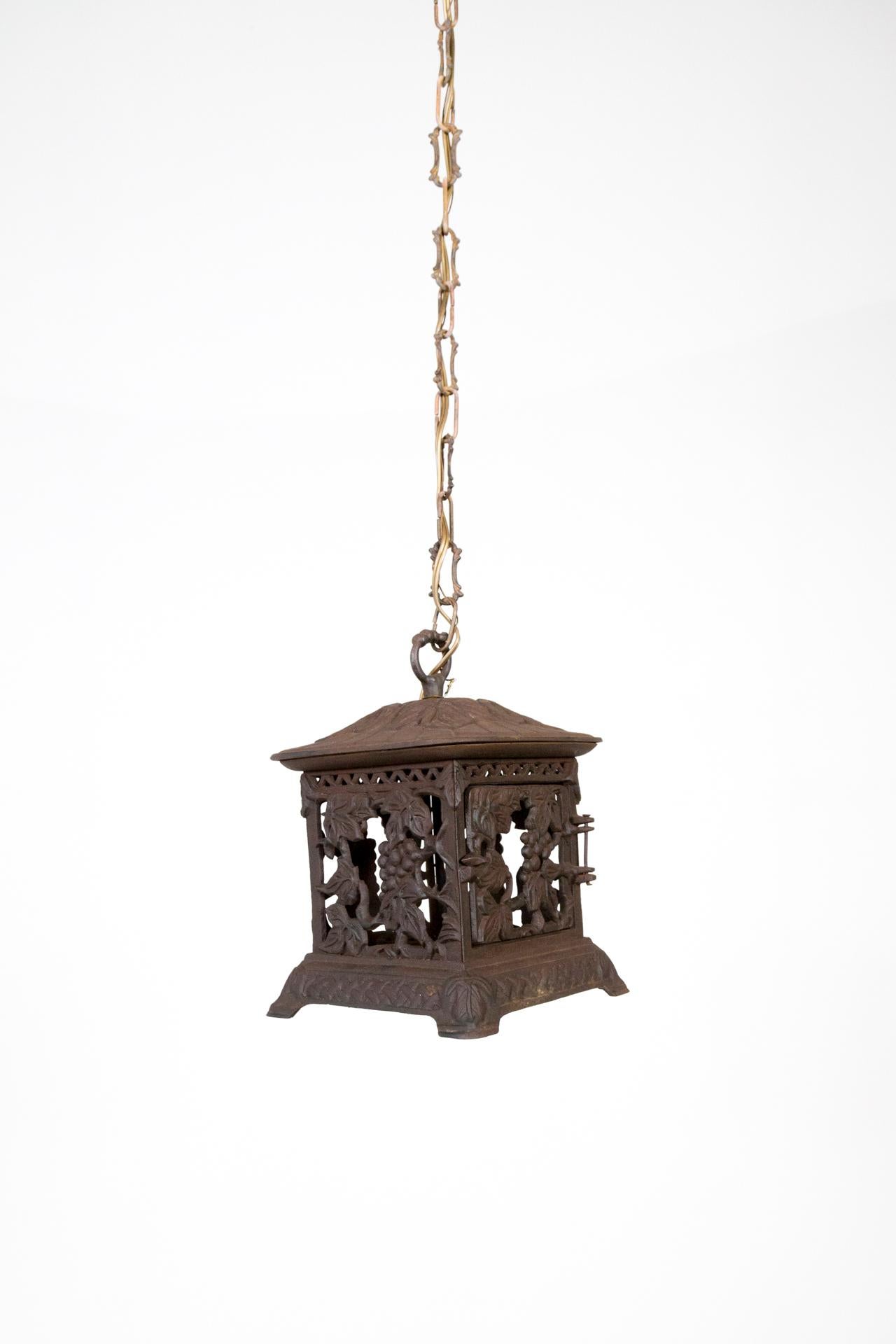 A pair of diminutive, vineyard themed, iron lanterns in a square shape with a base and a door. Newly wired into lanterns with decorative chains. One medium socket. Measures: 10” height x 7 x 7.