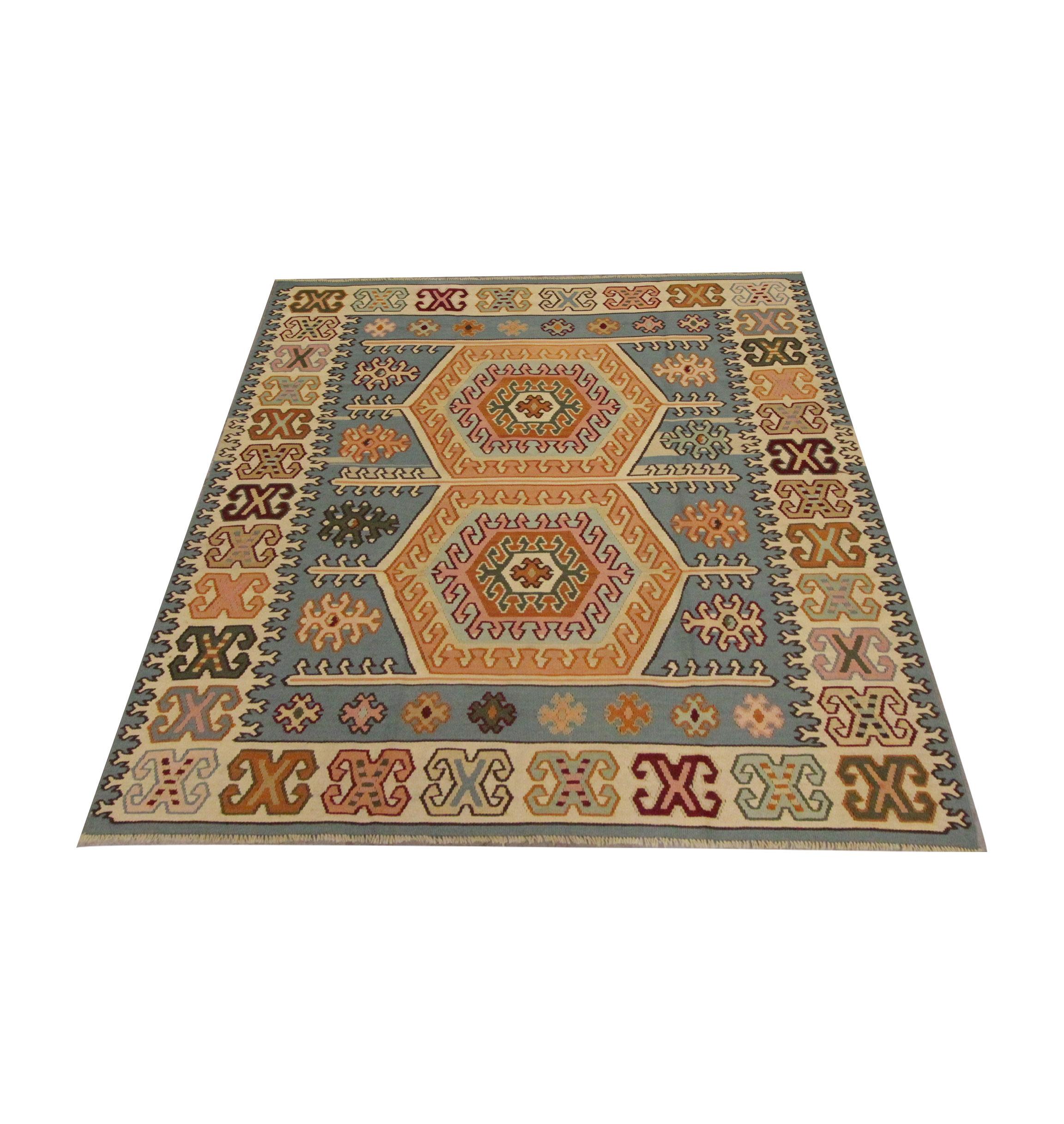 This small wool rug is a handmade Kilim woven in the early 20th century. The design has been woven in beige, rust-brown and blue accents on a subtle light-blue background. The bold tribal hook motifs and medallions pair beautifully with the colour