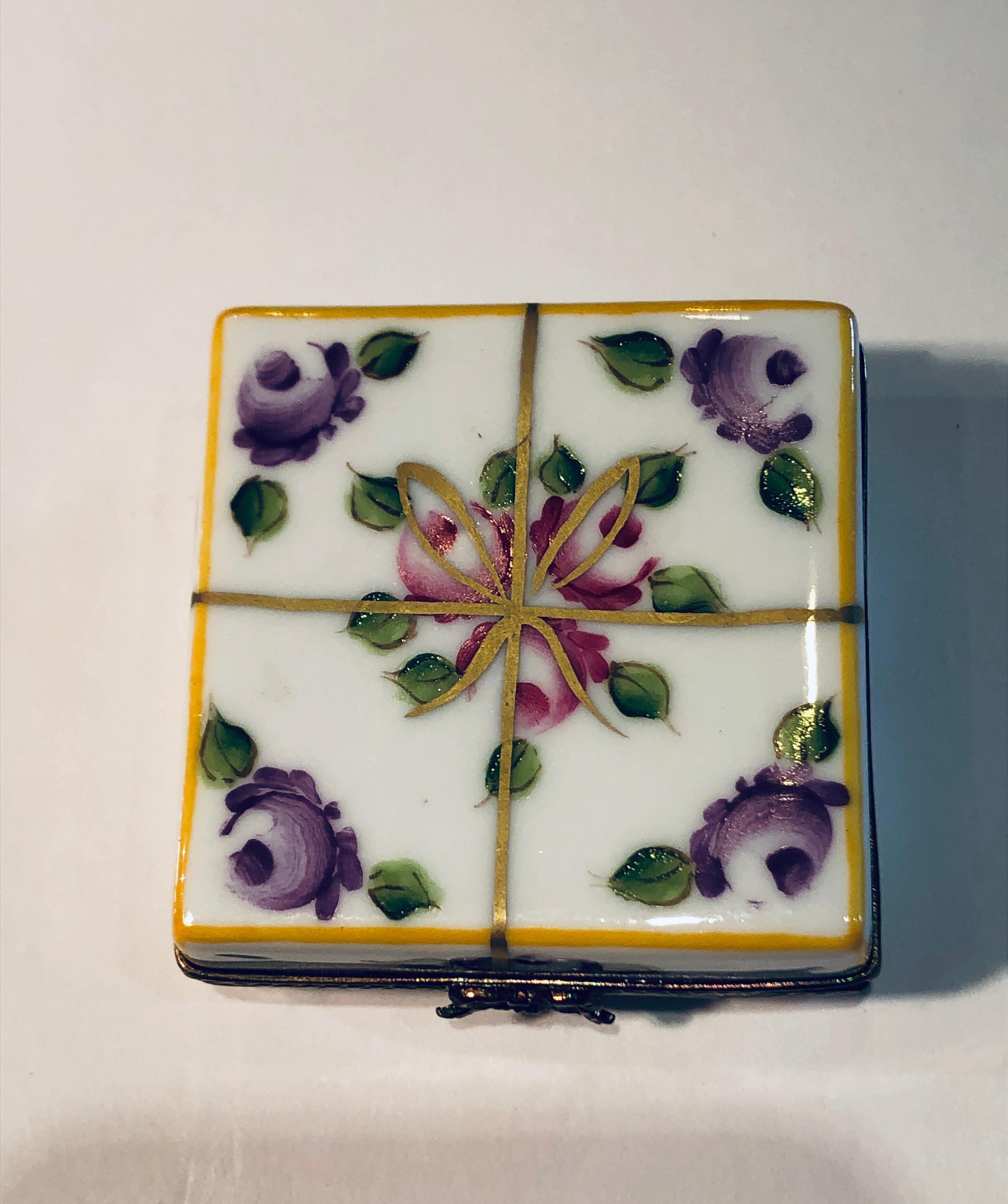 Collectible, limited edition Limoges porcelain miniature trinket box is handmade and hand painted with colorful roses, green leaves and a cheerful yellow border. It depicts a beautiful gift wrapped present which is tied with a painted, 24 karat gold