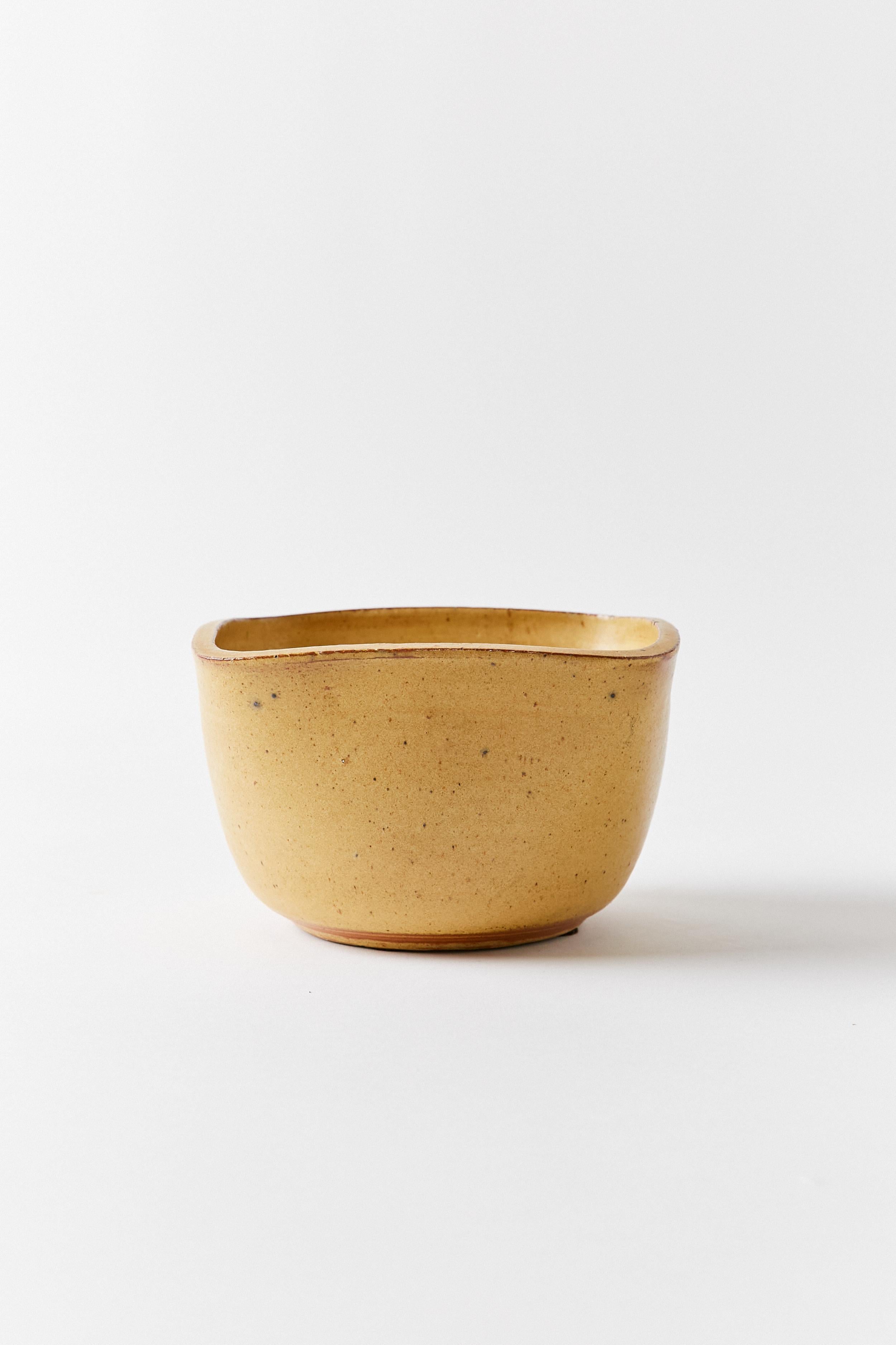 Square lip ceramic bowl in burnt yellow. The piece shows a fluid shape with round corners. Stamped NOA on the base.