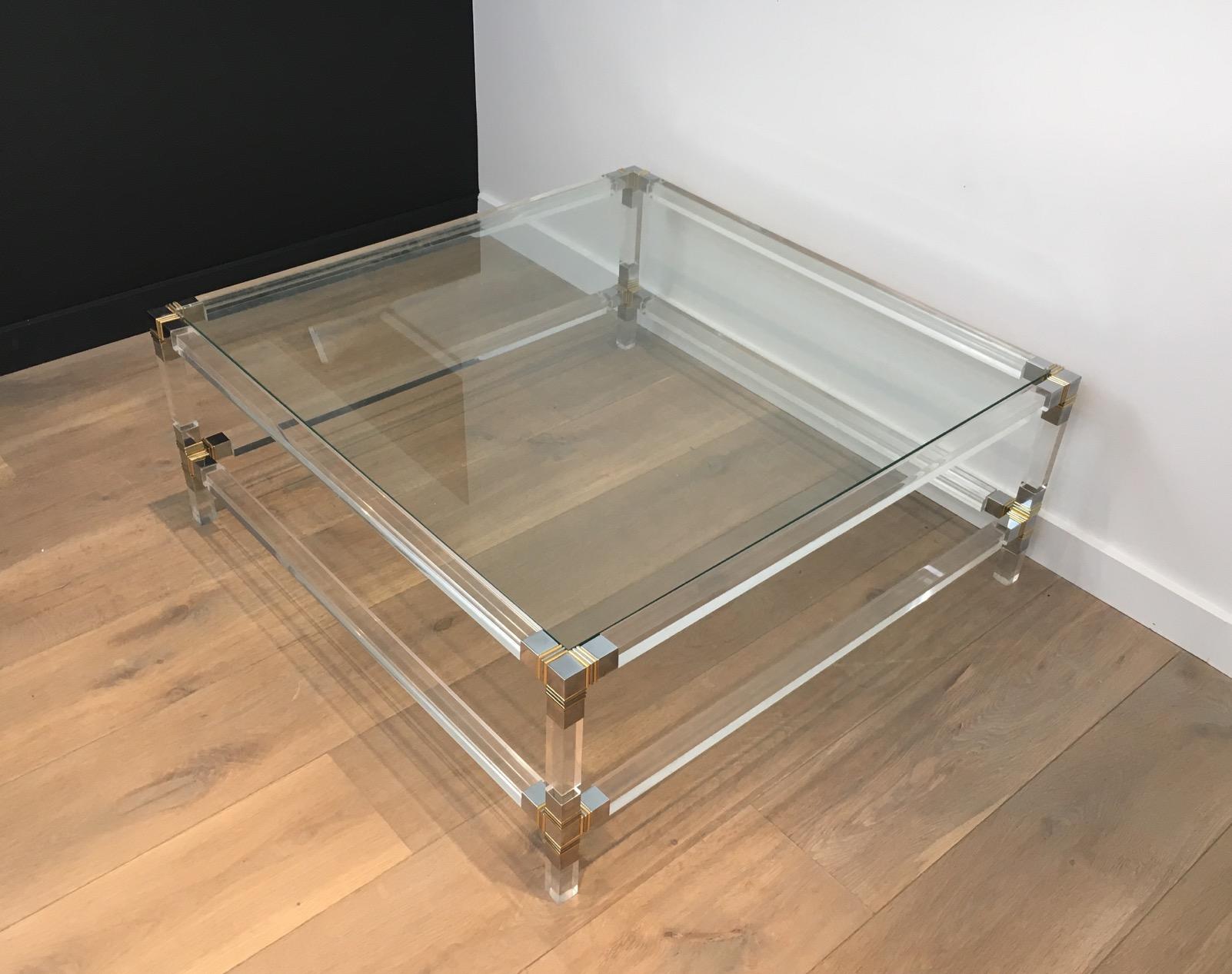 This square coffee table has a Lucite base with chrome and gilt chrome corners. Its two shelves are made of glass. This is a French design, from 1970s.