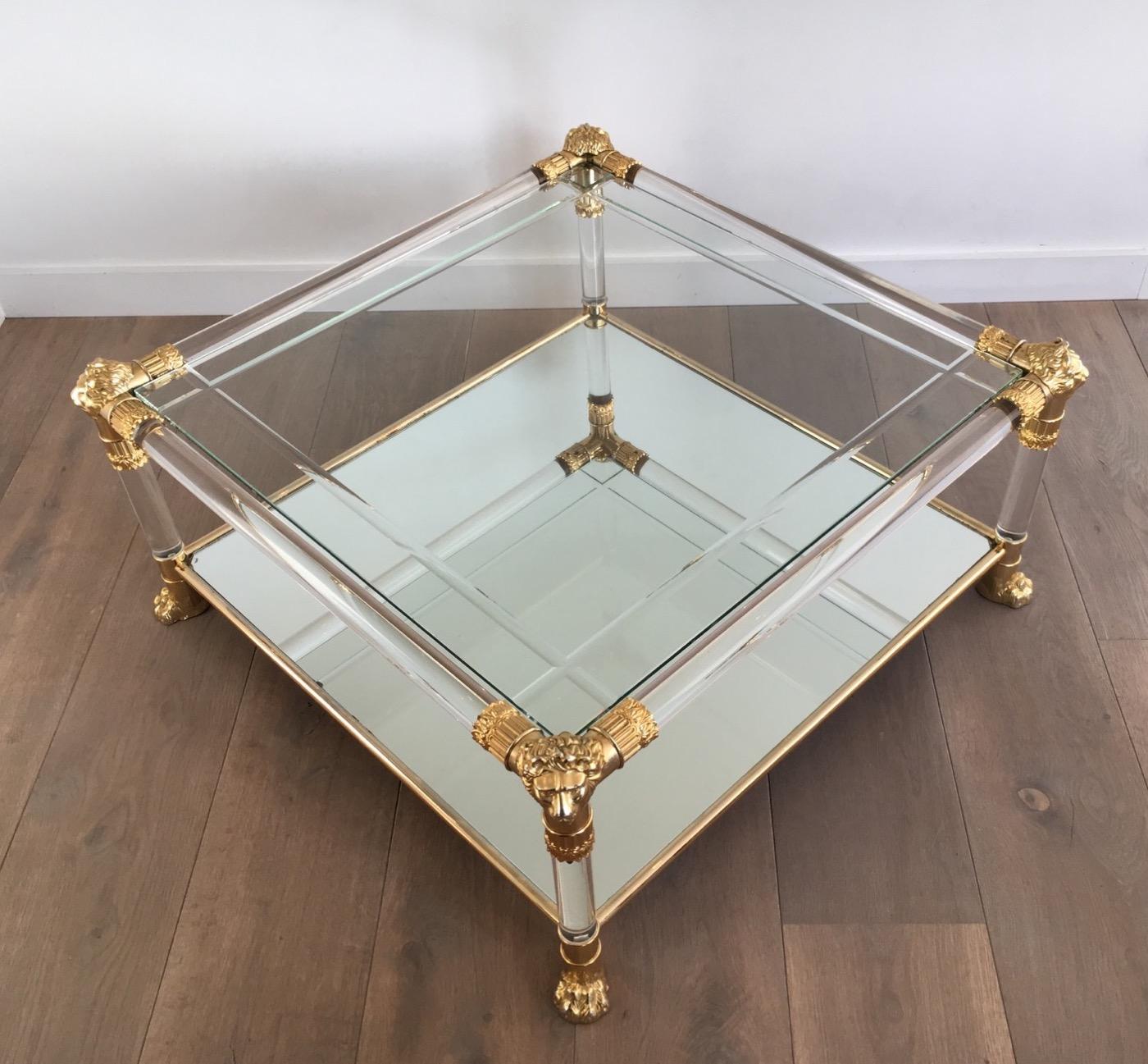 Square Lucite coffee table with gilt plastic lion heads and claw feet. The top shelf is made of engraved glass and the bottom shelf is a mirror. French, circa 1970.