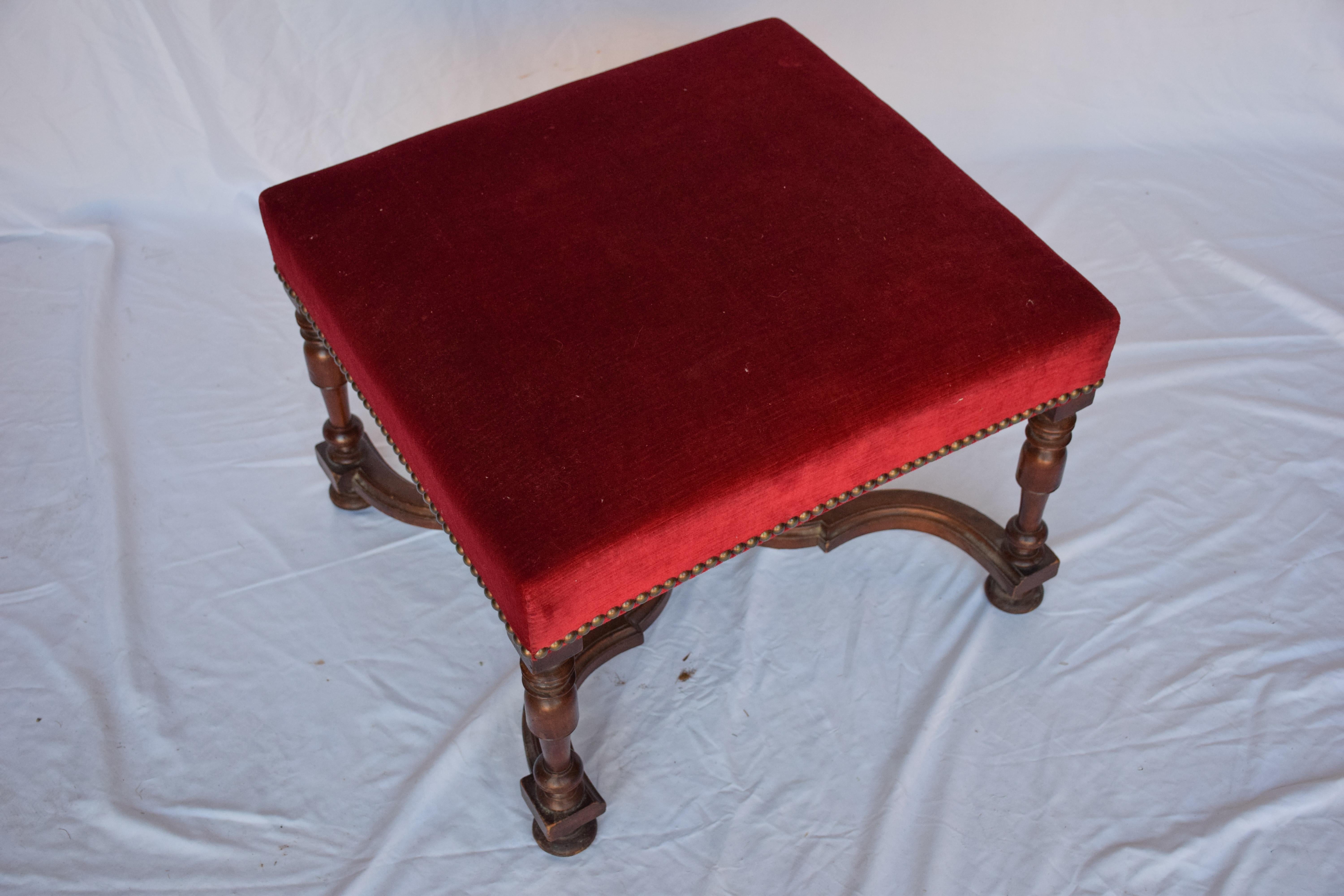 Beautiful Oak ottoman with upholstered top and nail trim. Burgundy velvet fabric in perfect condition. Antique brass tone nail trim around perimeter where fabric meets wood. With the added beauty of a finial, Stretcher bars are in great condition