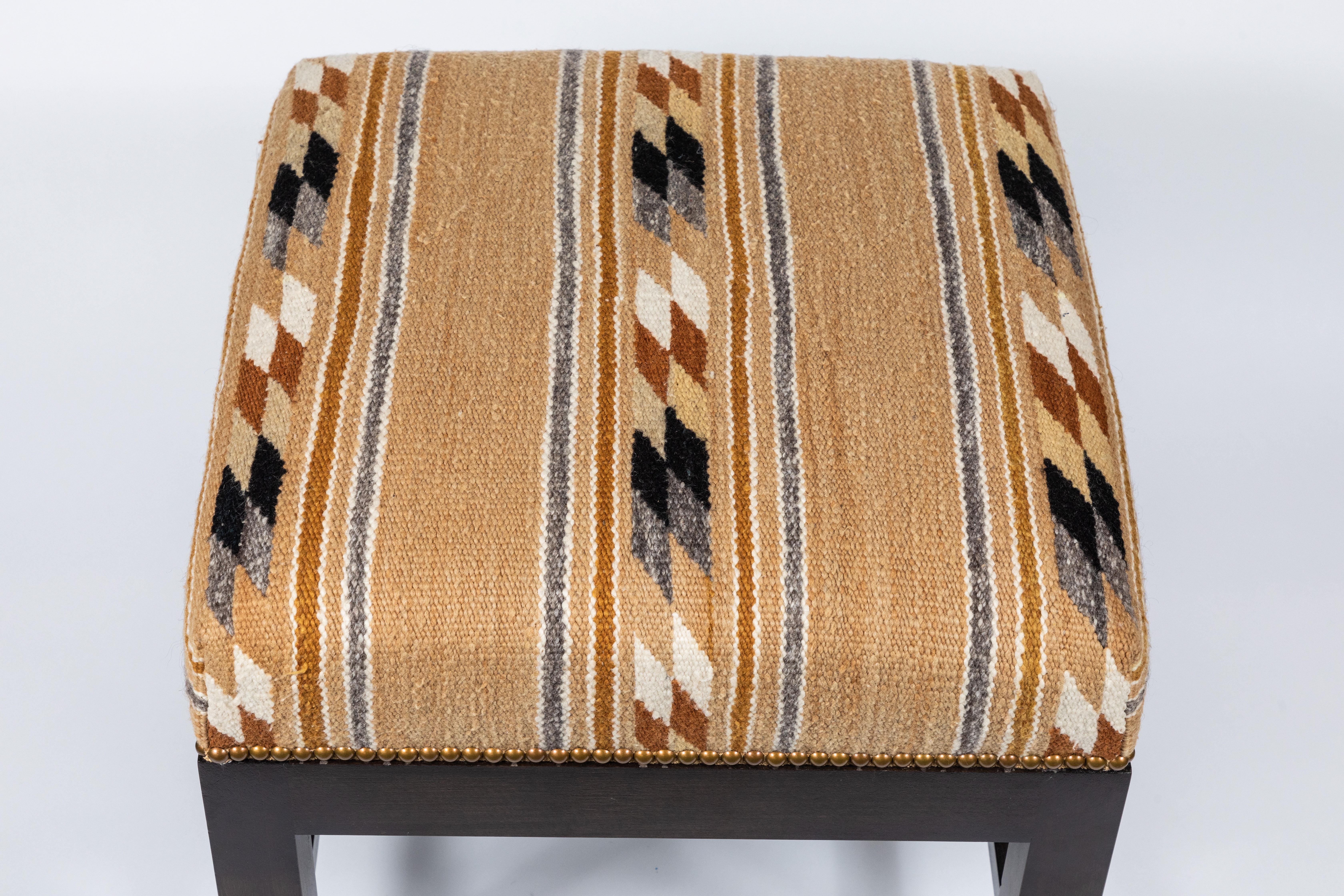 This is a new low stool upholstered in a vintage Native American rug textile in caramel, browns, and gold. This boxy ottoman can be seating or a table stool and features a walnut finish, stretchers, nailhead trim, and floor glides. 

* 1 available

