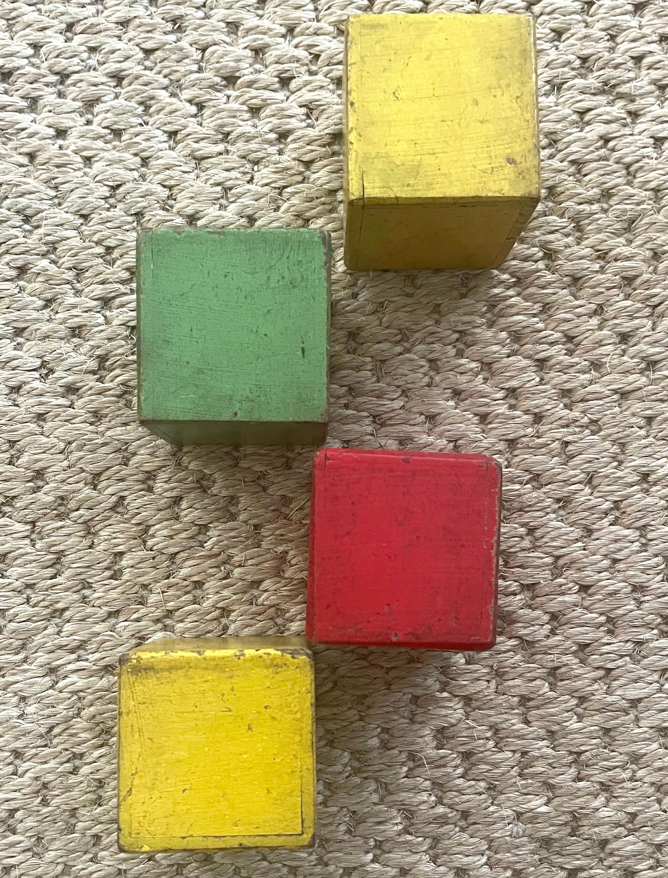 Quadratische bemalte deutsche Kinderrasselklötze aus Holz. Vier bemalte Holzklötze in den Farben gelb, rot und grün mit einem Rassel-Element im Inneren, das für Kleinkinder geeignet ist. Deutschland, 1930er Jahre
