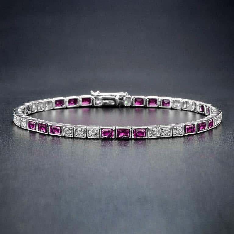Dieses atemberaubende Tennisarmband besteht aus quadratischen Rubinen, die jeweils von Brillanten umgeben sind. Das kühne, geometrische Art-Déco-Design schafft einen auffälligen Kontrast zwischen den tiefroten Rubinen und den funkelnden Diamanten.