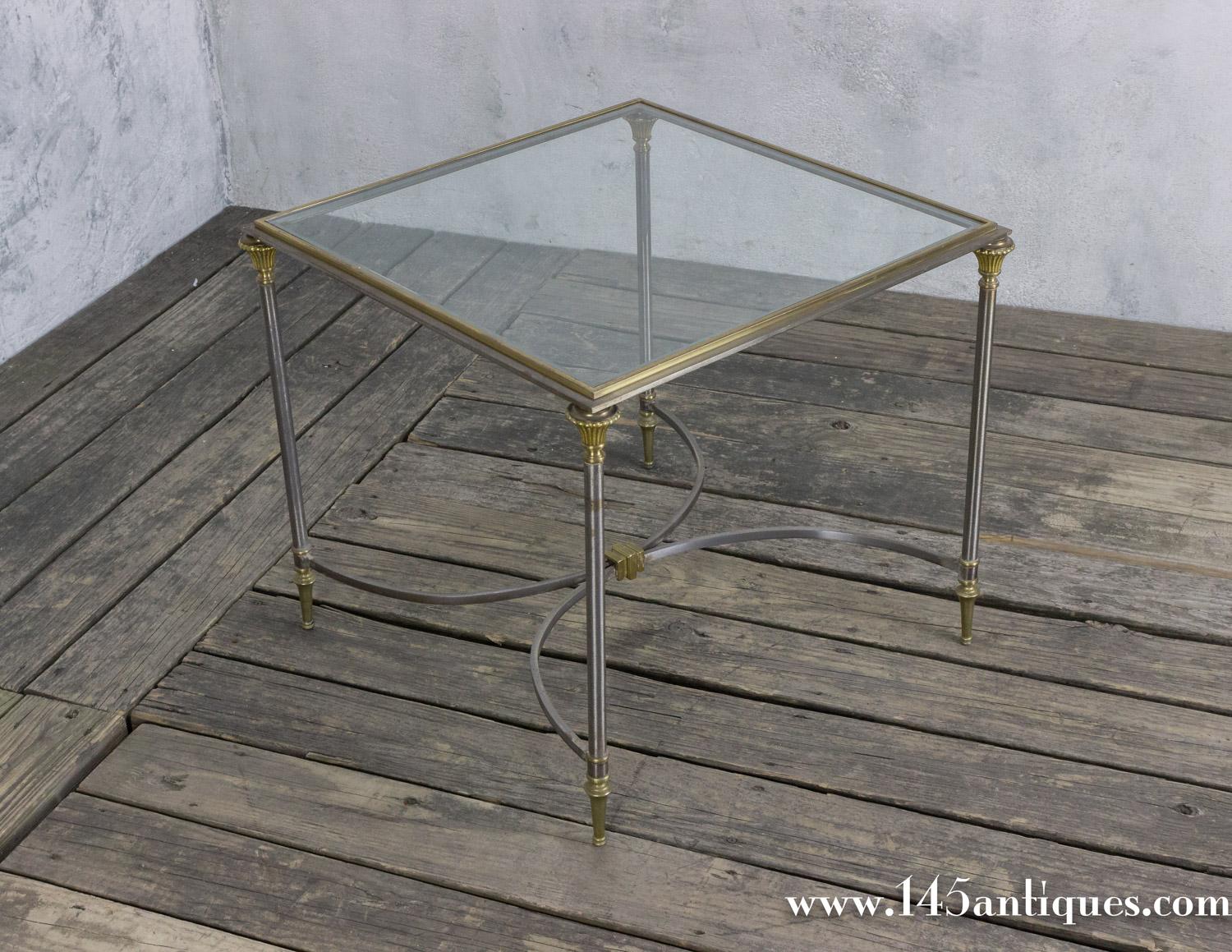 This square polished steel coffee table features brass highlights, a center stretcher, and an inset glass top. Reminiscent of the style of Maison Jansen, this table is believed to be Italian from the 1950s. In good vintage condition, this coffee