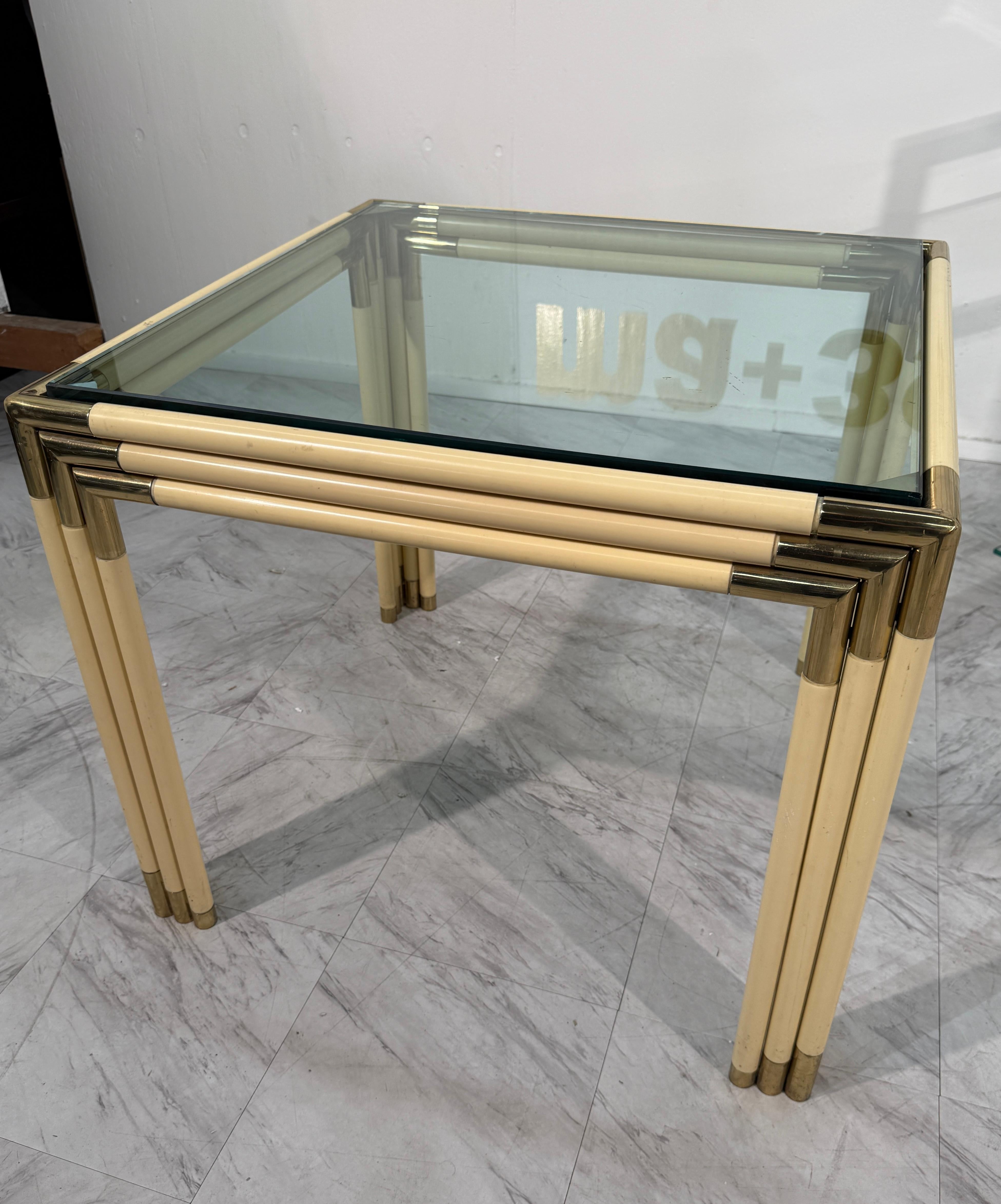 Elégante table d'appoint italienne moderne du milieu du siècle dernier, datant des années 1970, dotée d'un plateau carré en verre soutenu par un cadre en faux-bambou en laque crème avec des accents plaqués laiton. Le design tubulaire superposé du