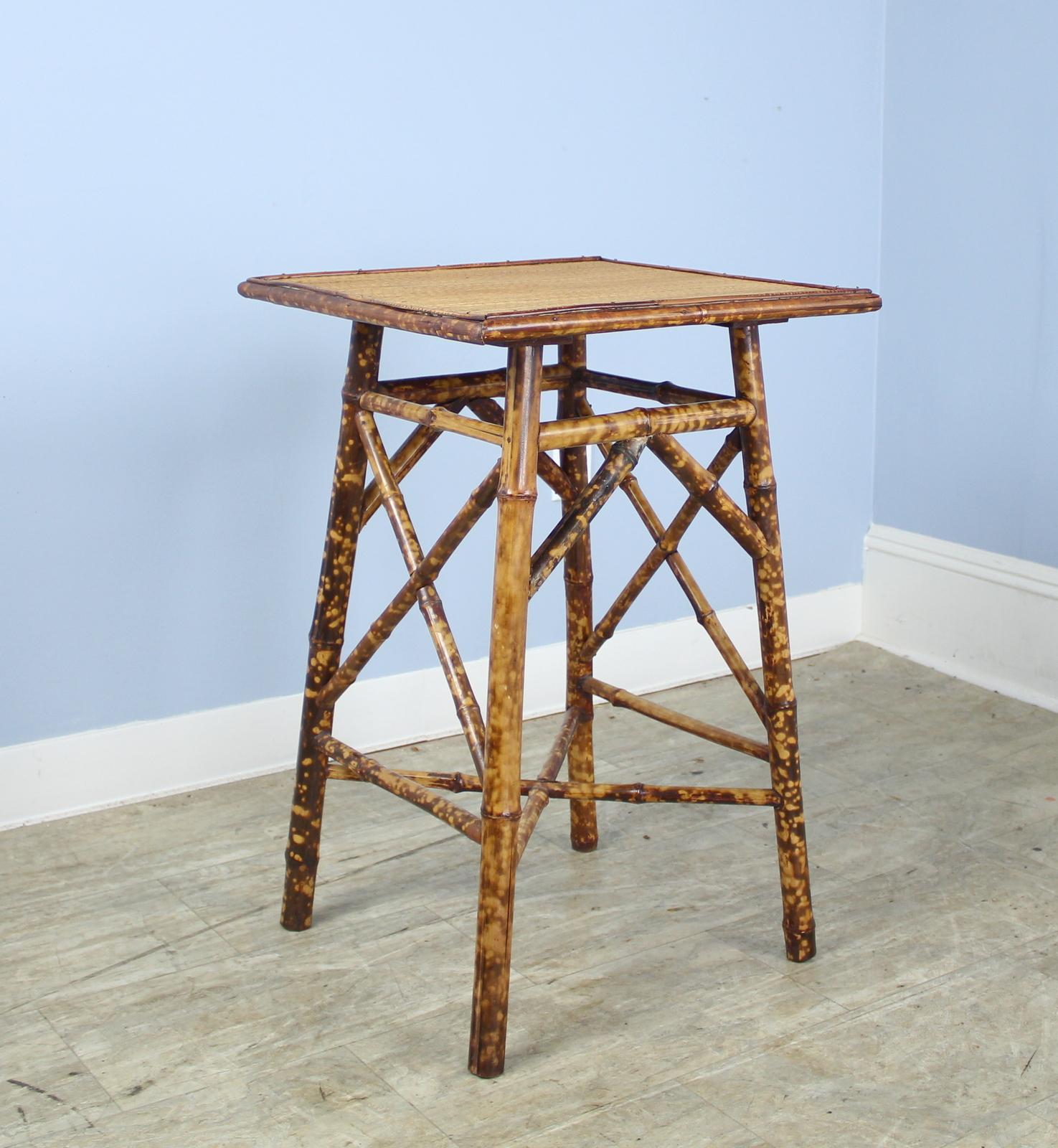 An antique English bamboo side table, with flared legs and with two shelves. Highly decorative decorative details on all sides. Both shelves are made of tightly woven rattan that is in very good condition. The bamboo, vividly painted, is in good
