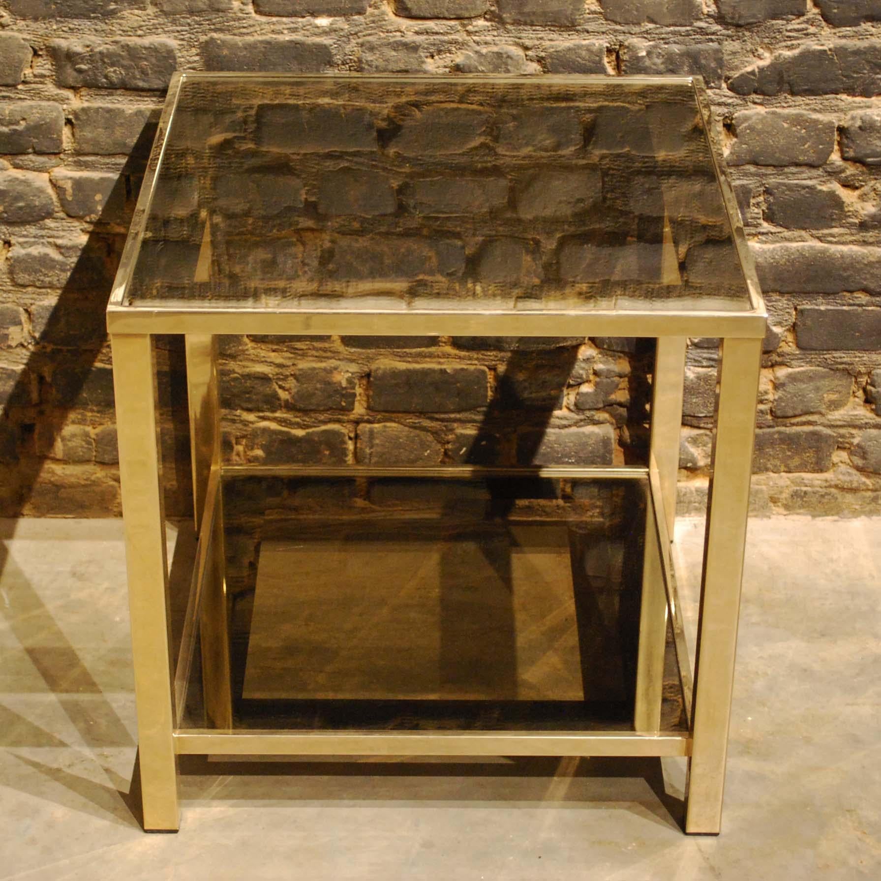 This beautiful side table was made in the early 1980s by Belgian Belgo Chrom. 
The table has a metal frame that was gold plated with a thin layer of 23-carat gold. The table features two smokey glass plates with a dark surround. The legs are