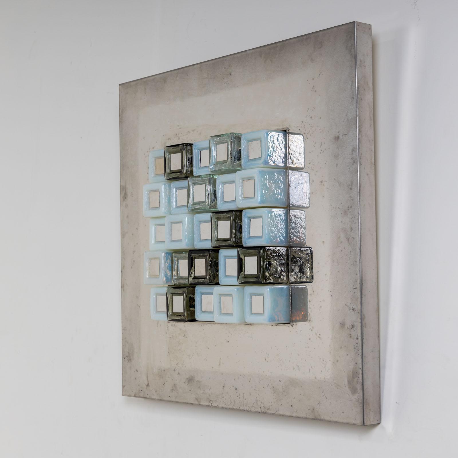 Illuminated wall object designed by Angelo Brotto (1914-2002) in the 1970s for Esperia. This unique lamp comprises a square metal plate and additional Murano glass blocks arranged in the center. The cubes are crafted from clear, opaque, and green