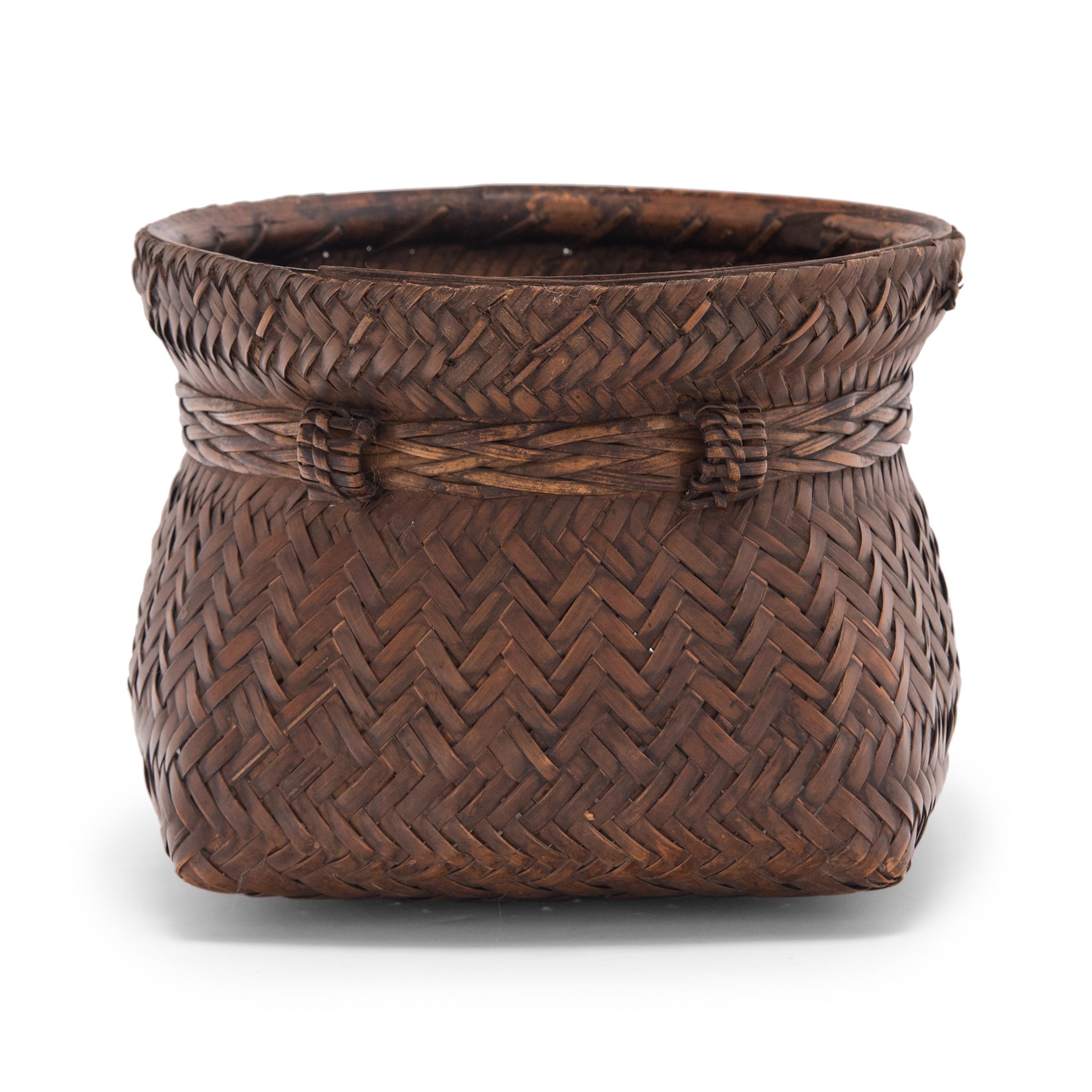 This vintage square basket is beautifully woven of thin strips of smoked bamboo in alternating diagonal twill patterns. The woven sides are secured to a rigid bamboo frame at the opening and cinched by a braided band for a more defined shape.