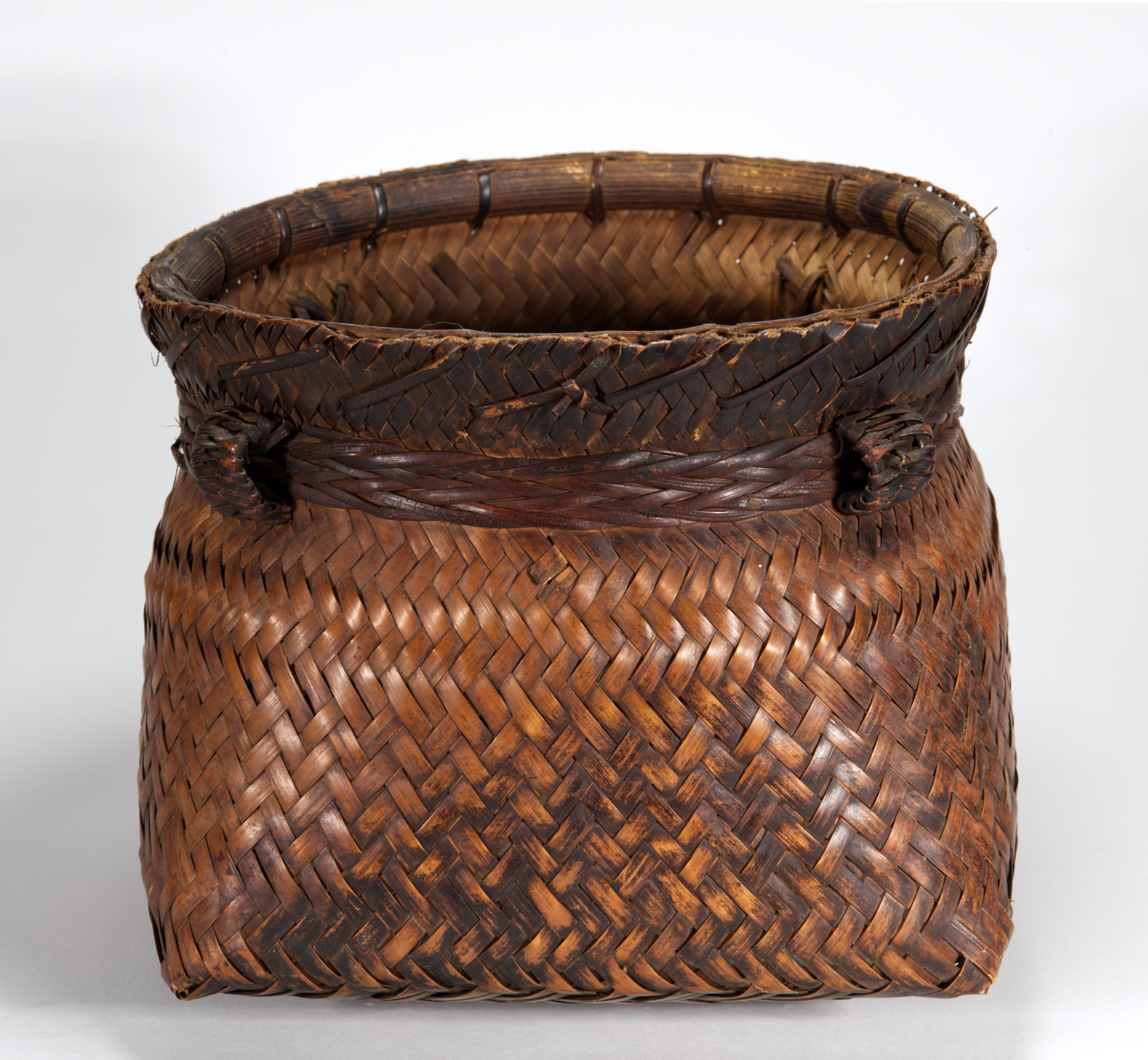  Vintage Philippine Folk Art open basket features square-shaped bottom and circular top. The body is plaited of darkened with smoke brown fibers in complex, intricate chevron pattern. The waist of the basket is decorated with woven rattan strip with