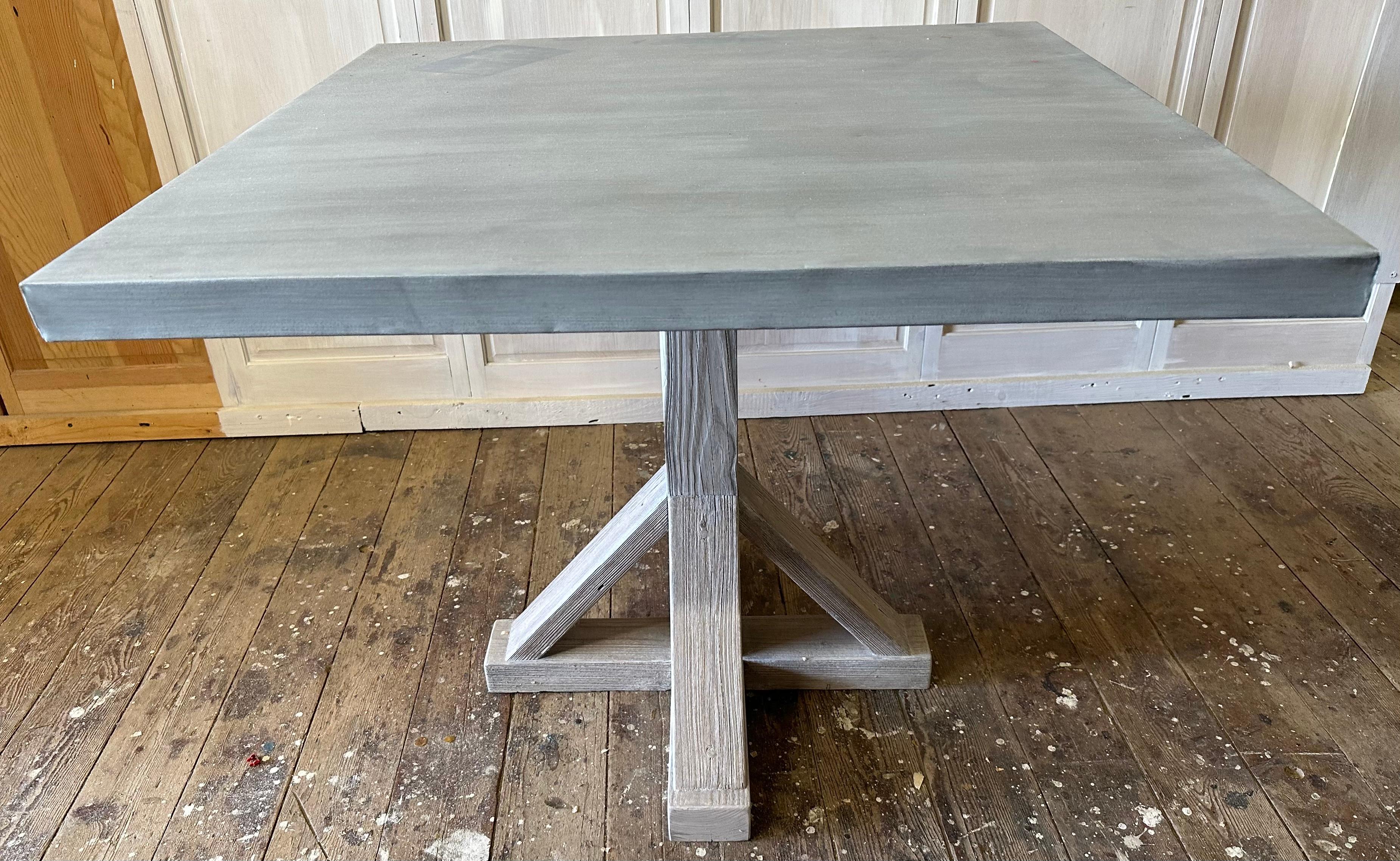 A timeless Swedish Gustavian inspired farmhouse table made with square zinc table top and a white washed wood pedestal table base. The table makes a perfect addition to any kitchen or dining room. Natural and rustic in appearance, will be suitable