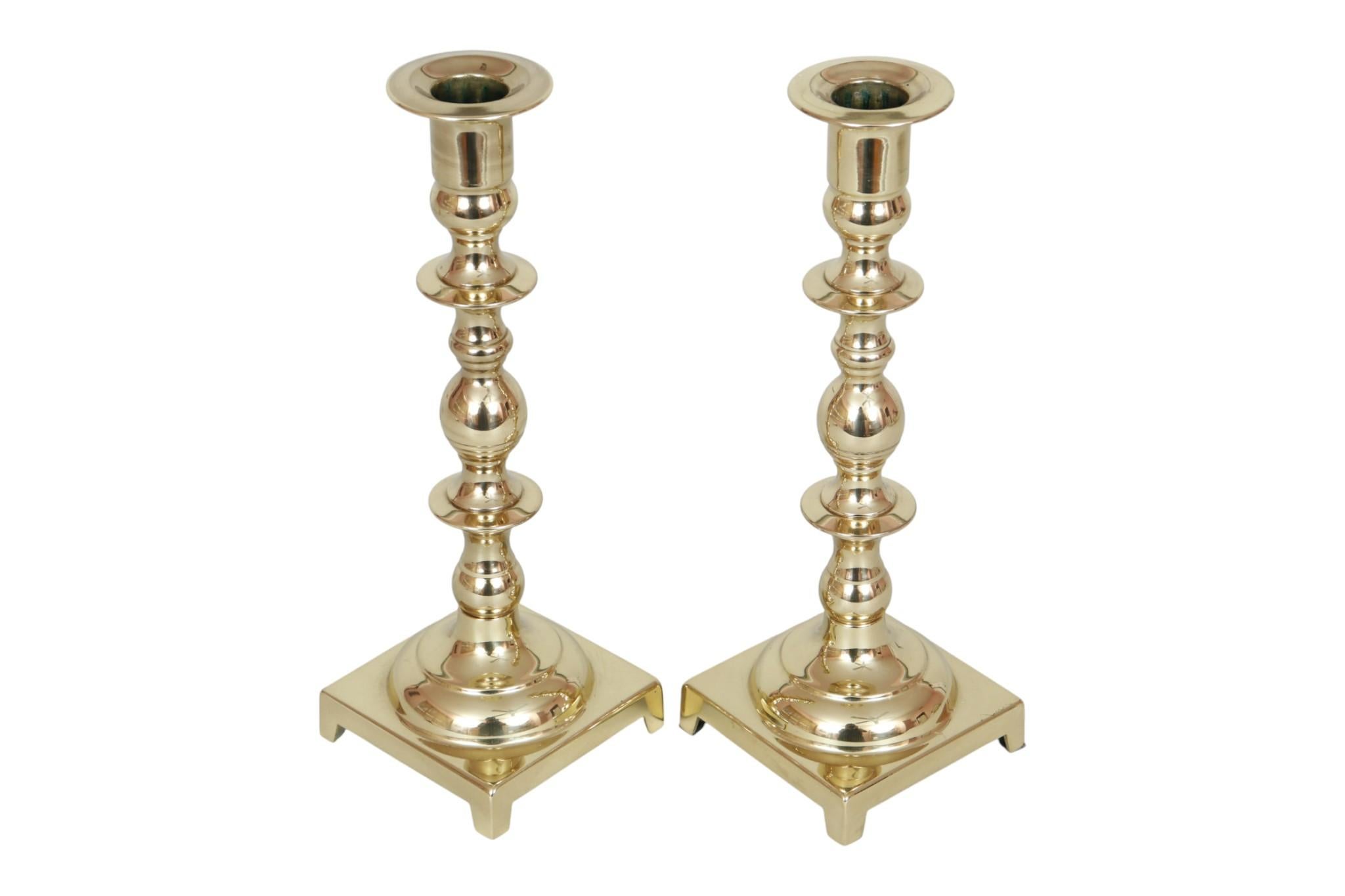 A pair of traditional style gold brass candlestick holders circa 1950. Sleek capitals top turned columns, decorated with several knops, above square bases raised on small bracket feet. Dimensions per candlestick holder.