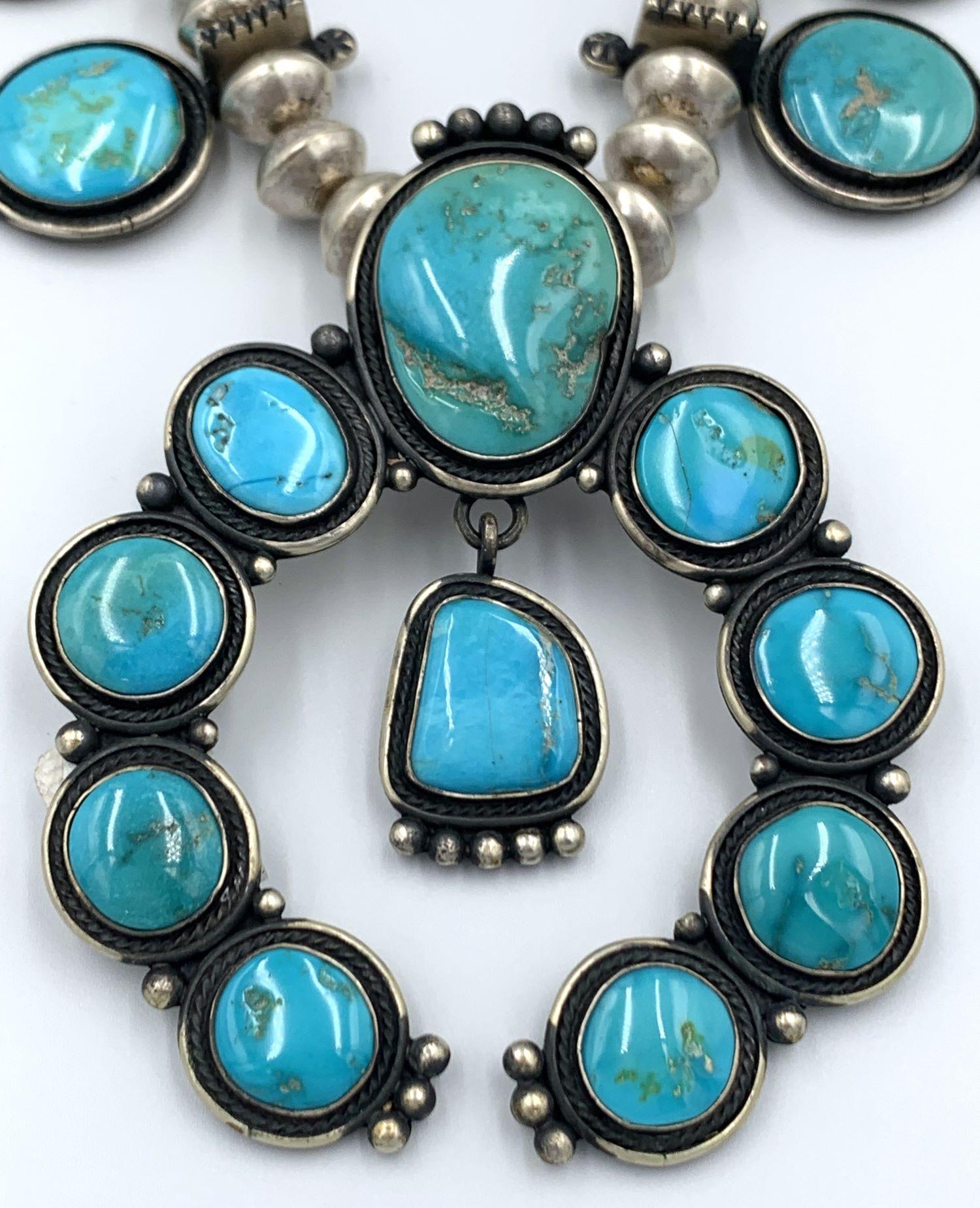 Sterling silver Navajo squash blossom necklace by award winning Navajo silversmith Tommy Jackson. The 27” necklace is comprised of 12 squash blossoms with a Blue Gem turquoise and a naja made up of 10 Blue Gem turquoise set in sterling silver. The