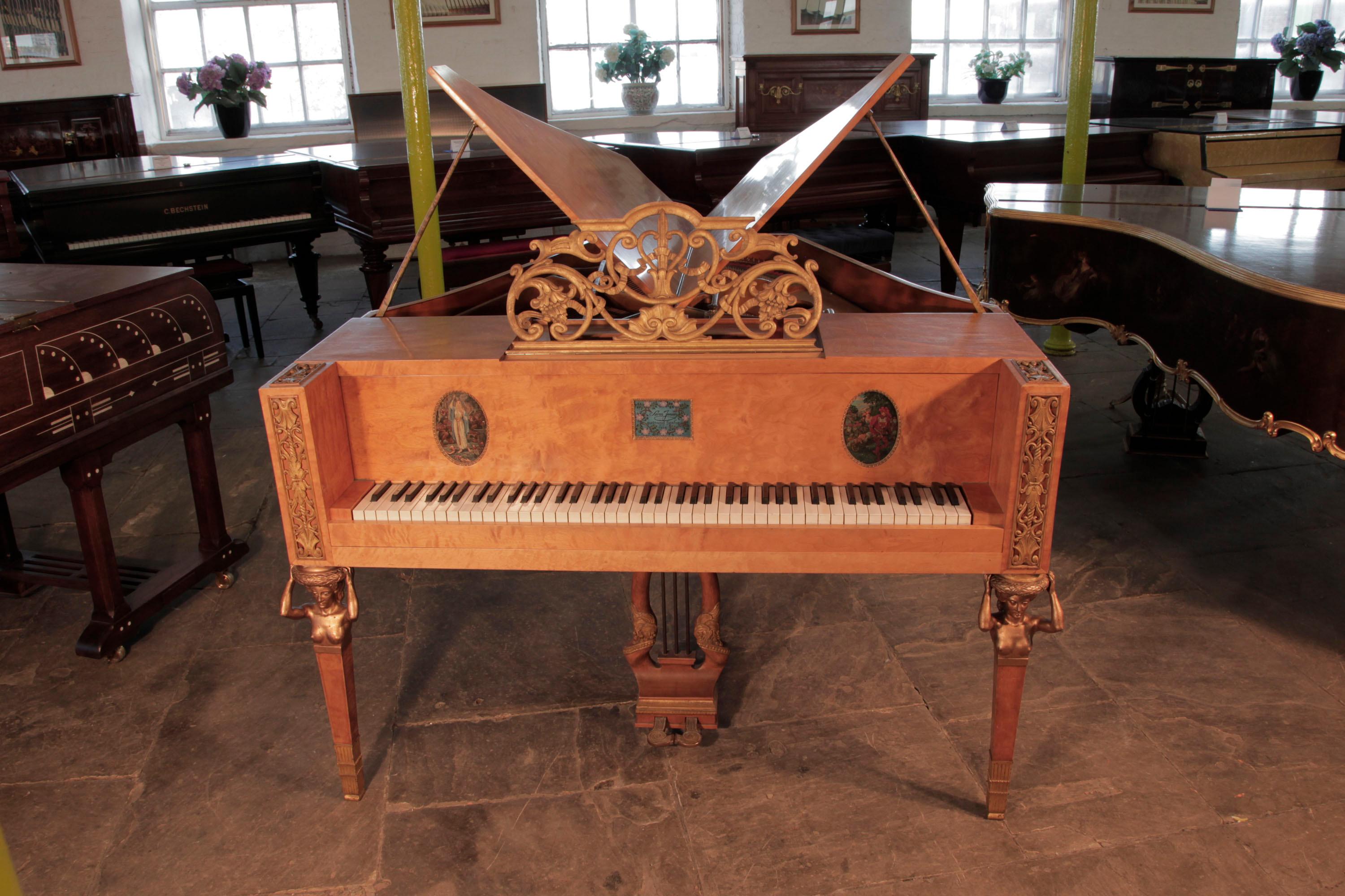 

A 1918, Søren Jensen model D butterfly grand piano with a polished, maple case. The gilt music desk is in an openwork, scrolling design featuring flowers, shells amd swags. Piano sits on three square, tapered legs with bronze female nude,