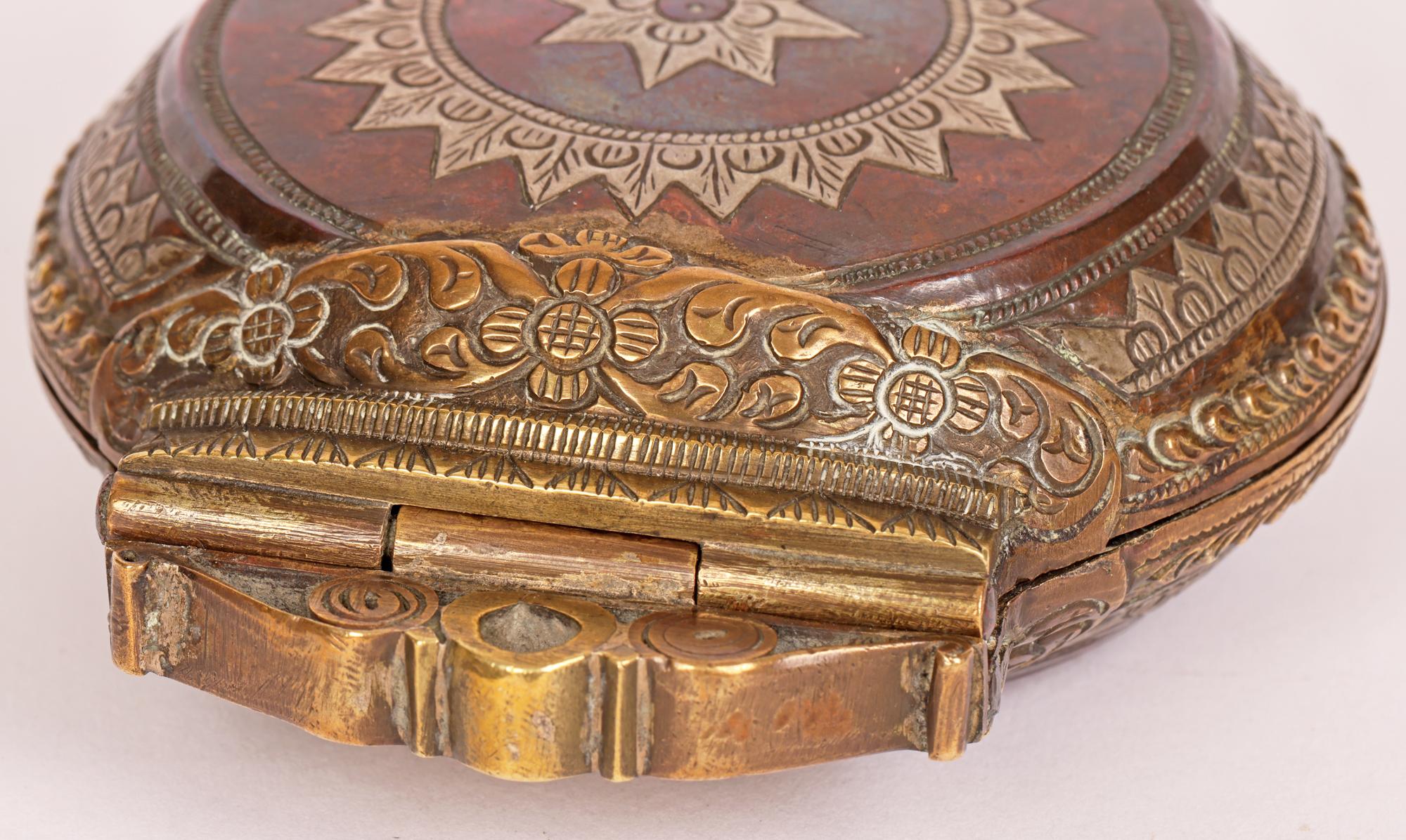 A good quality antique Sri Lankan copper and brass betel lime box with silver inlay and floral applications dating from the 18th or 19th century. Known in Sri Lanka as a Killotaya the box is of flattened round form with an ornate scroll work hinged