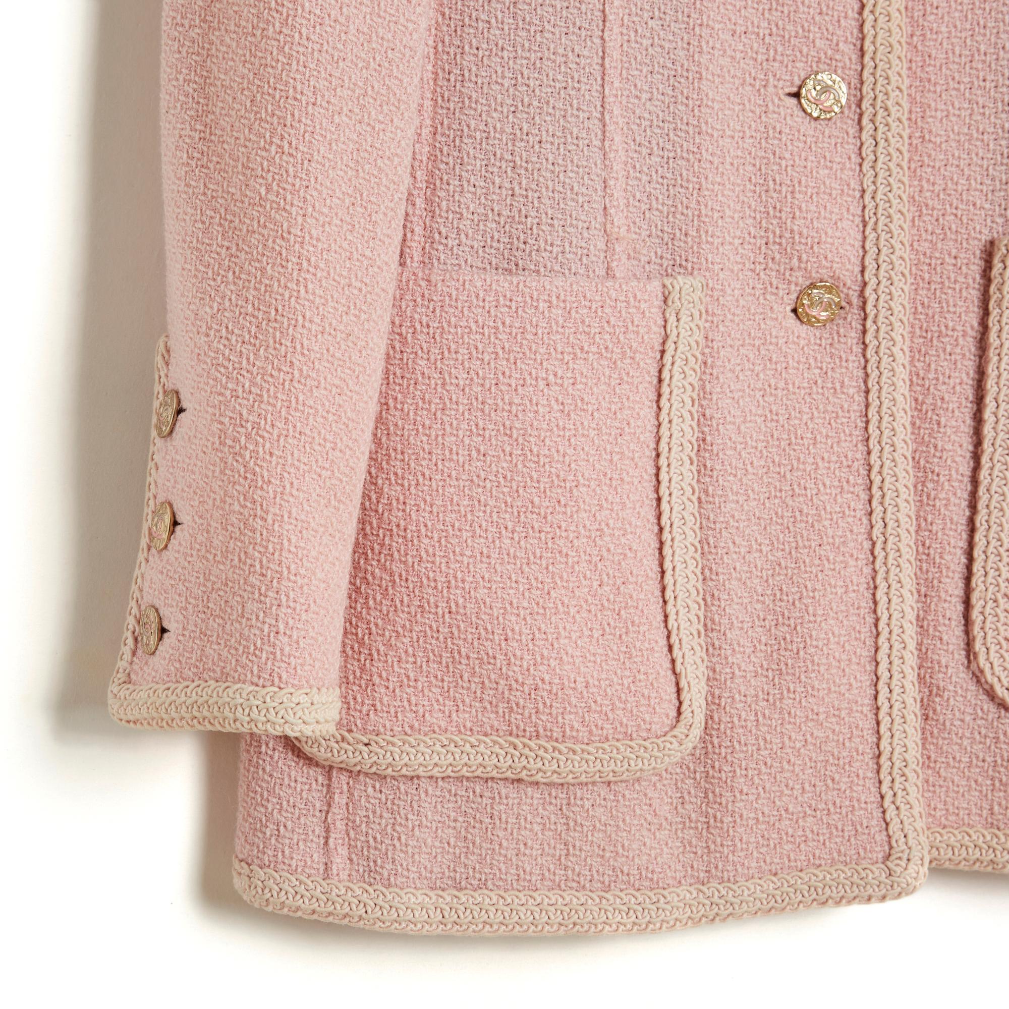 Veste Chanel circa 1994 en laine mate rose pâle garnie de passementerie beige écru, col rond fermé par 6 boutons de la marque Chanel en métal légèrement doré, 4 poches plaquées sur la poitrine et sur les hanches, manches longues fermées chacune par