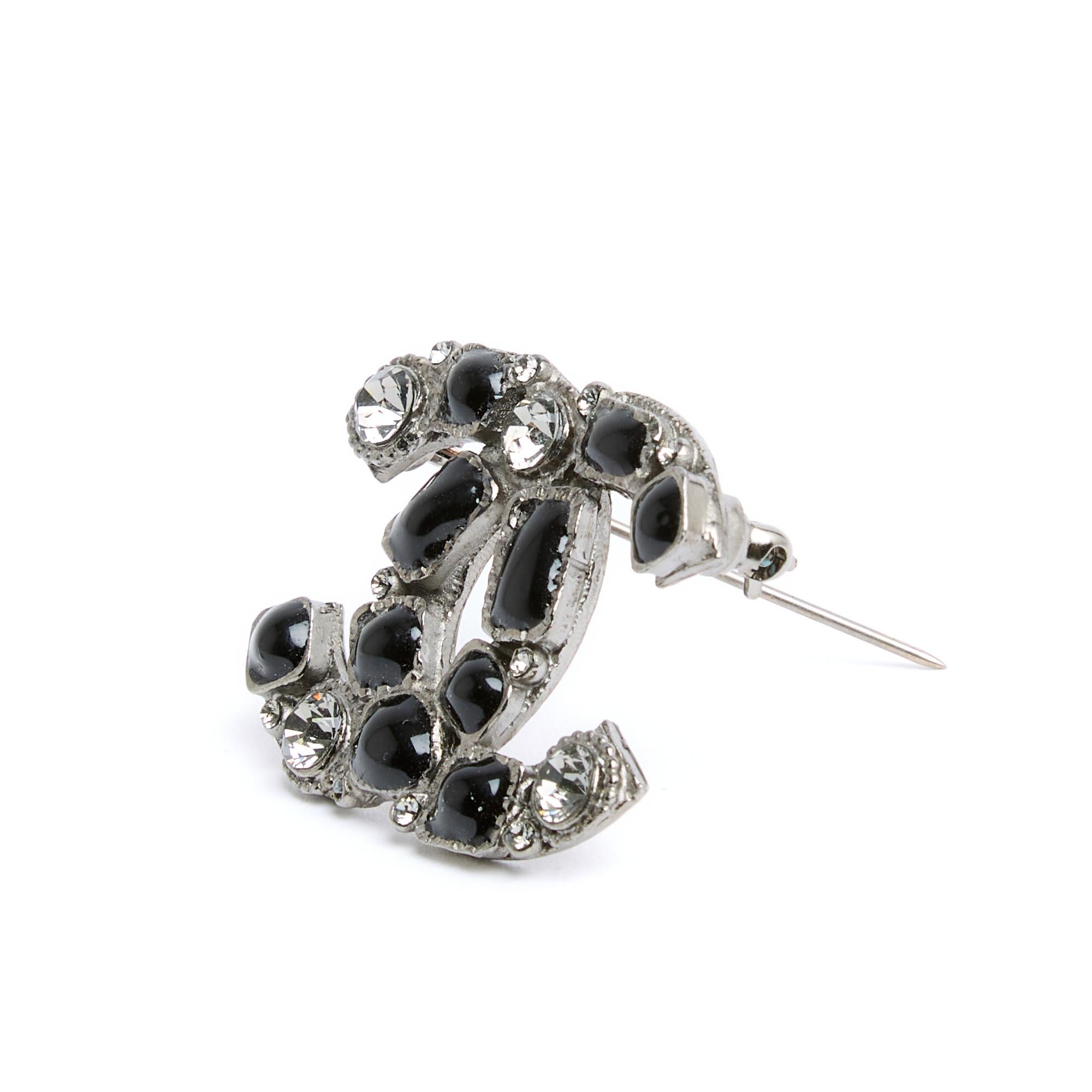 Chanel-Brosche aus der Collection'S Spring Summer 2009 mit dem CC-Logo-Motiv aus geschwärztem, silbernem Metall, verziert mit grauen Strasssteinen und schwarz emaillierten Cabochons. Breite 3,7 cm x Höhe 2,9 cm. Die Brosche wird ohne