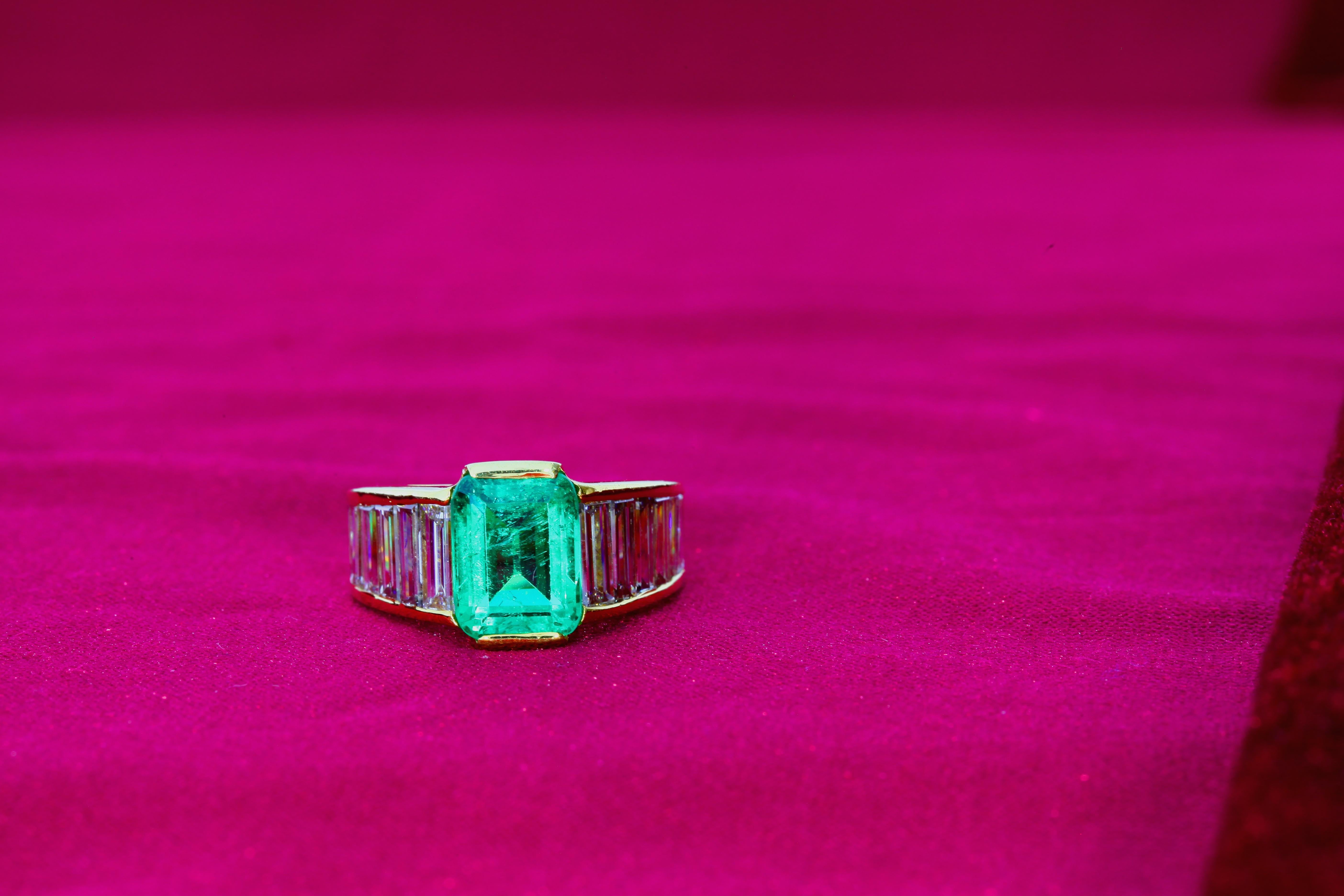 This SSEF Certified Colombian Emerald with minor oil treatment is set in a 18 karat gold ring and flanked by twelve tapered baguette-cut diamonds. The color of the emerald is green of medium saturation. 