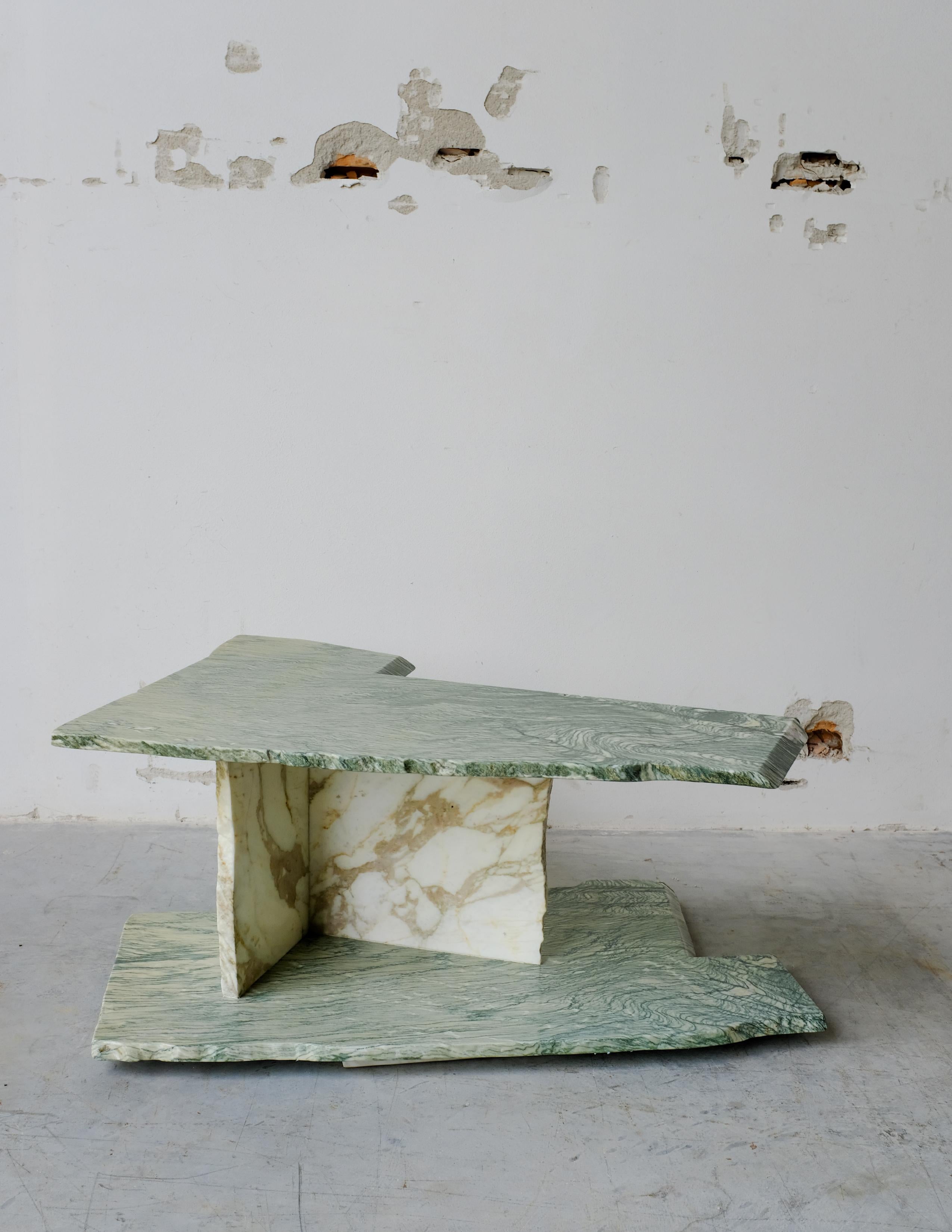 This coffee table features two main Cipollino Verde marble slabs, which are admirably shaped directly by previous productions. These two slabs are connected to each other by two elements in Calacatta Oro marble. The coarse finish and the randomness