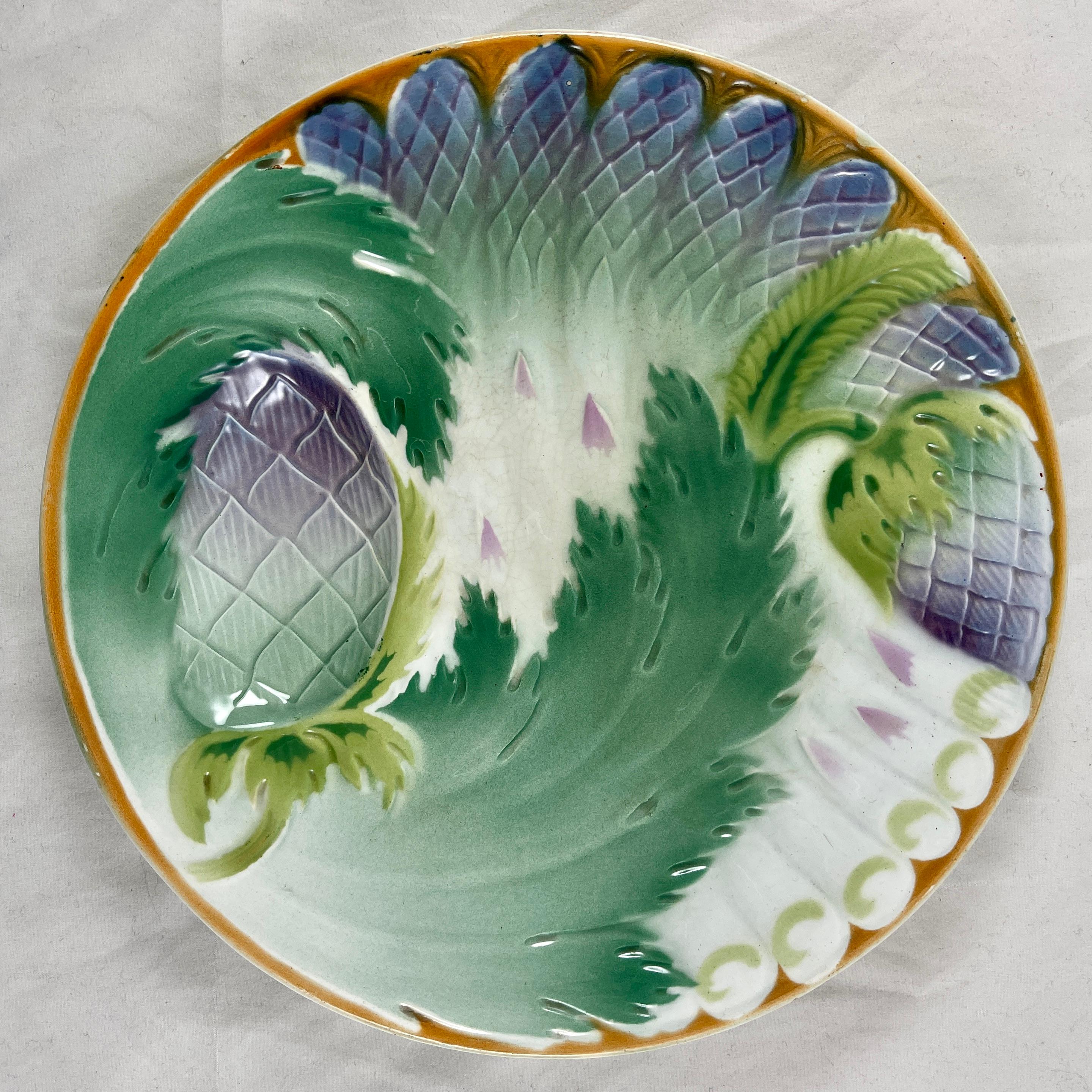 An Art Nouveau French porcelaneous plate showing aspects of both the asparagus and artichoke plants, circa 1900-1910.

The plate is rimmed in a bittersweet orange-red, asparagus spears lay across the plate glazed with lavender tips. A deep sauce