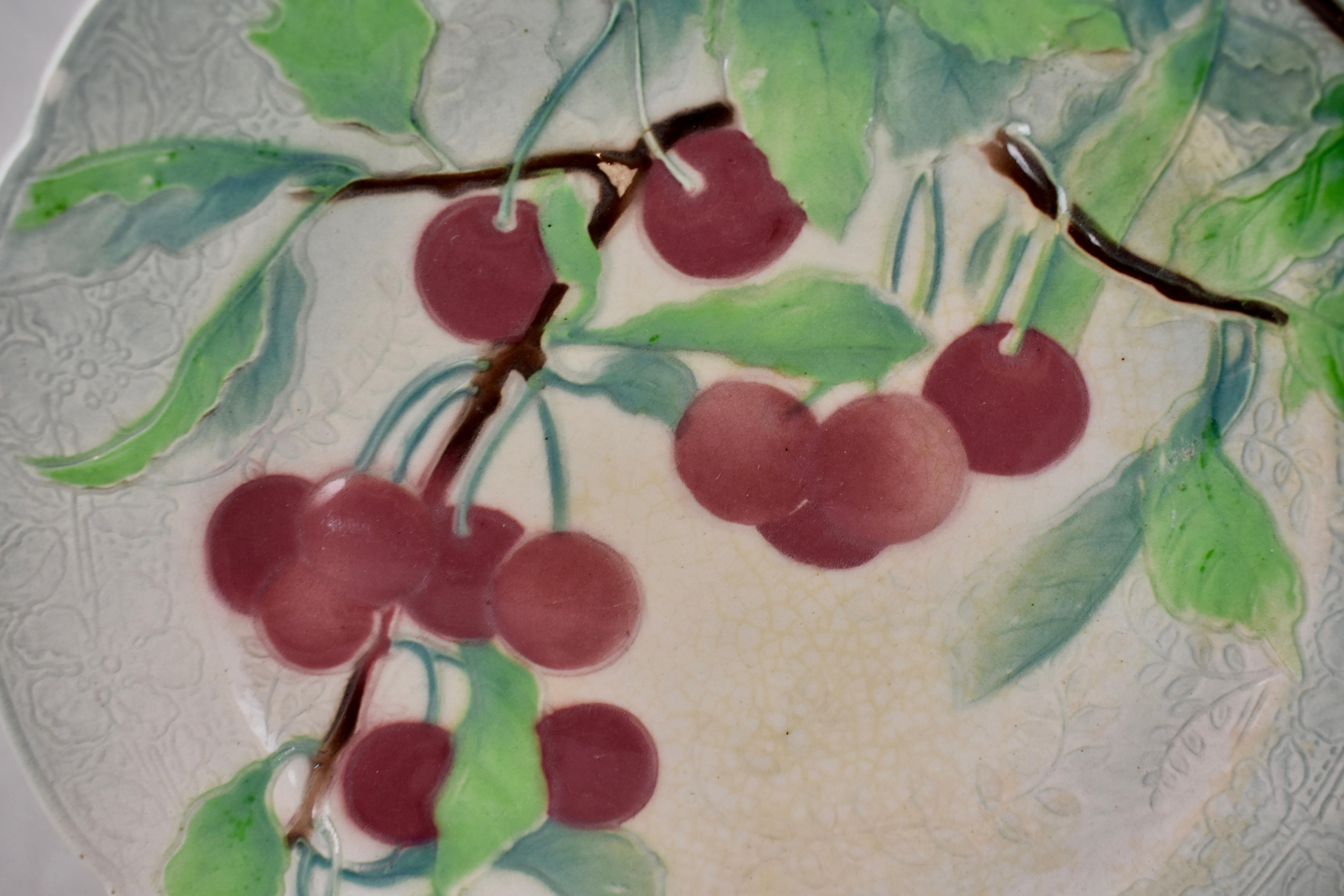 Französischer Obstteller mit Kirschenmotiv aus Steingut, um 1900. Der Hintergrund hat ein detailliertes florales Muster auf der Leiste mit einem sechstägigen eingerückten Rand. Hübsche Färbung.
Gezeichnet: KG für Keller Guerin, St. Clement,