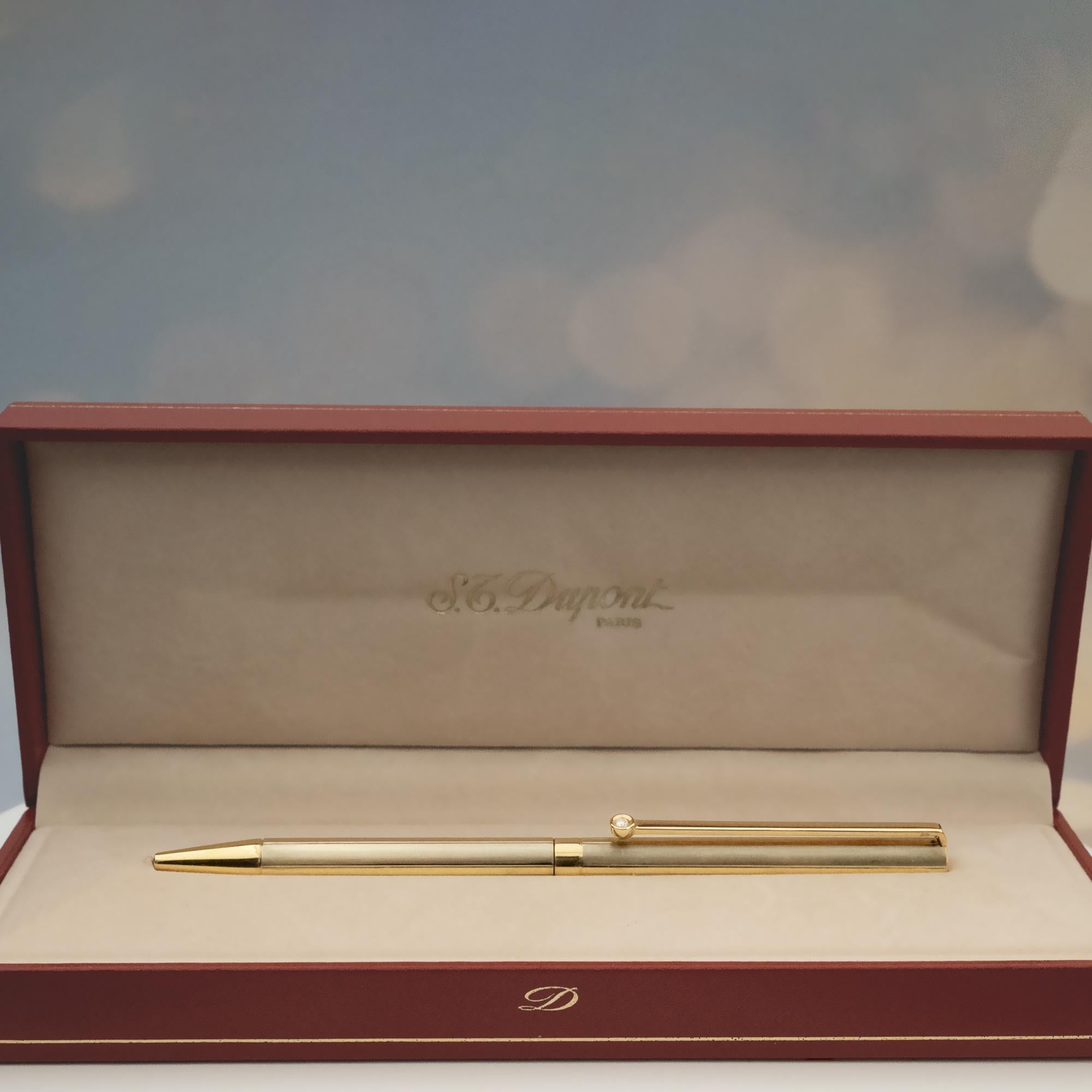 Este S.T. El bolígrafo Dupont, ofrecido por Claris-A, está fabricado en oro blanco y amarillo de 18 quilates, y presenta la elegante silueta característica de Dupont, con un cuerpo liso y aerodinámico. Un único diamante engastado en el clip añade un