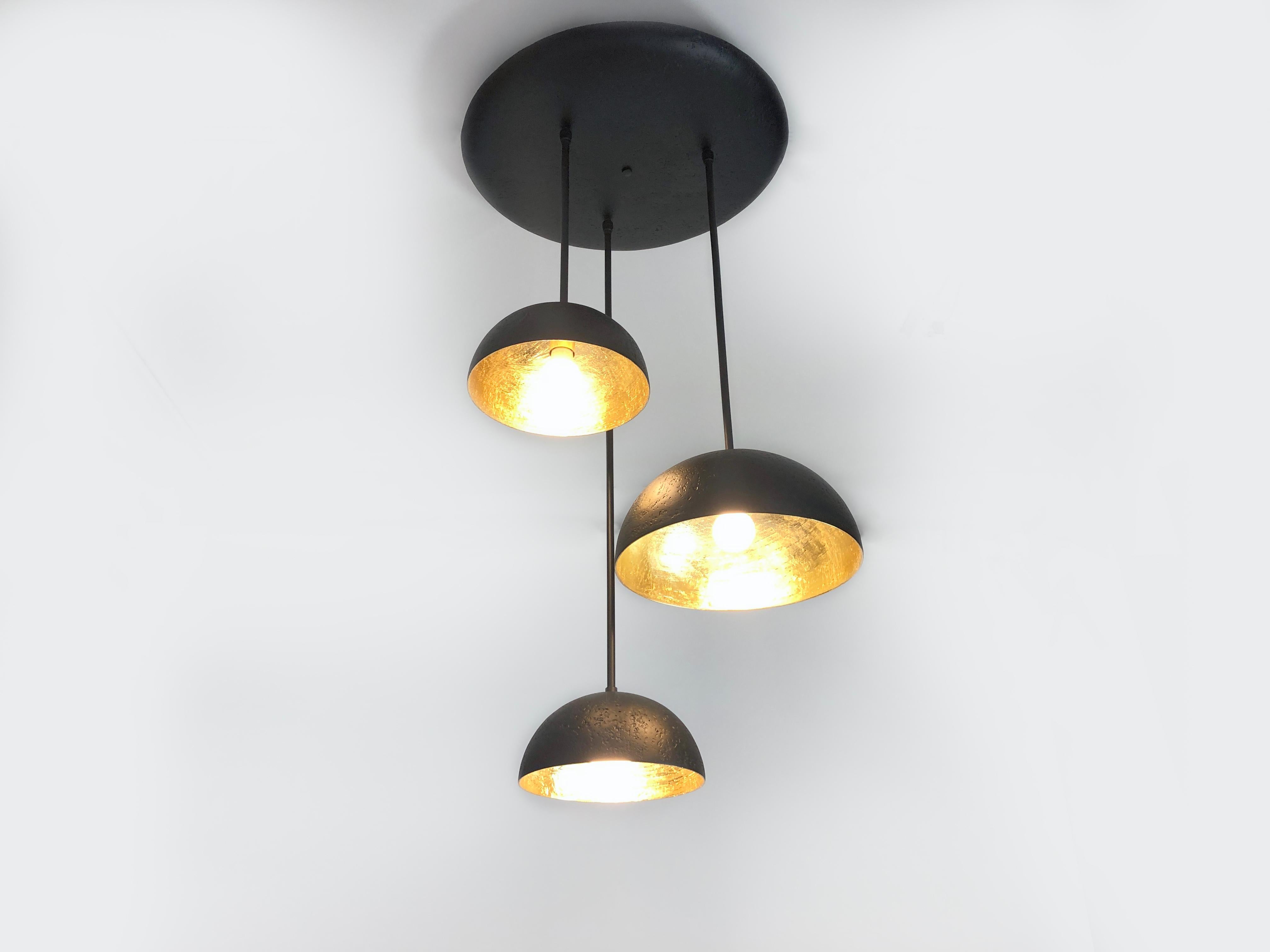 Three pendant chandelier. The finish of the hand crafted plaster of Paris domes and canopy are matte black. This accents the gold leafed interiors of the domes. This chandelier can be customized to work for each project. Light uses three medium